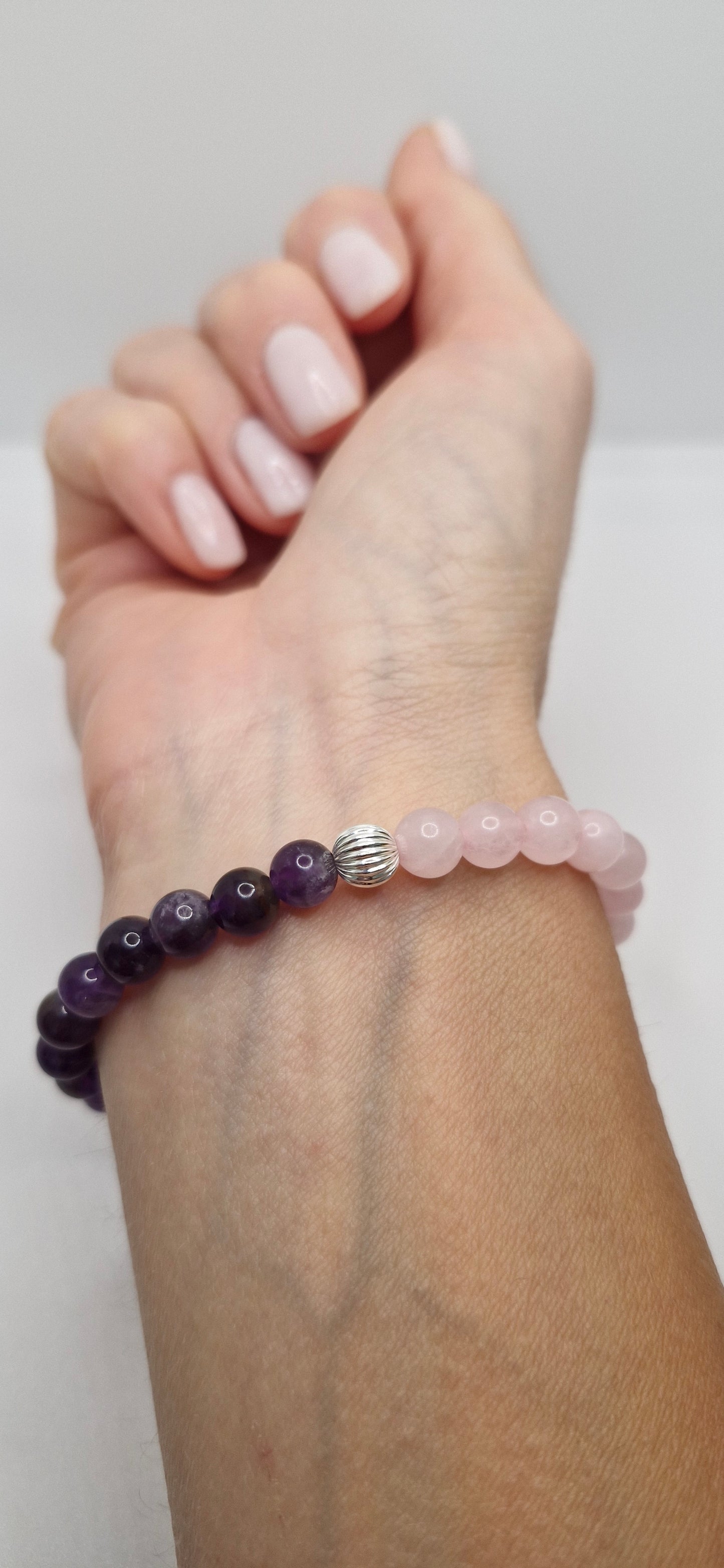 Hand wearing a pink beaded bracelet with a silver charm on a plain background