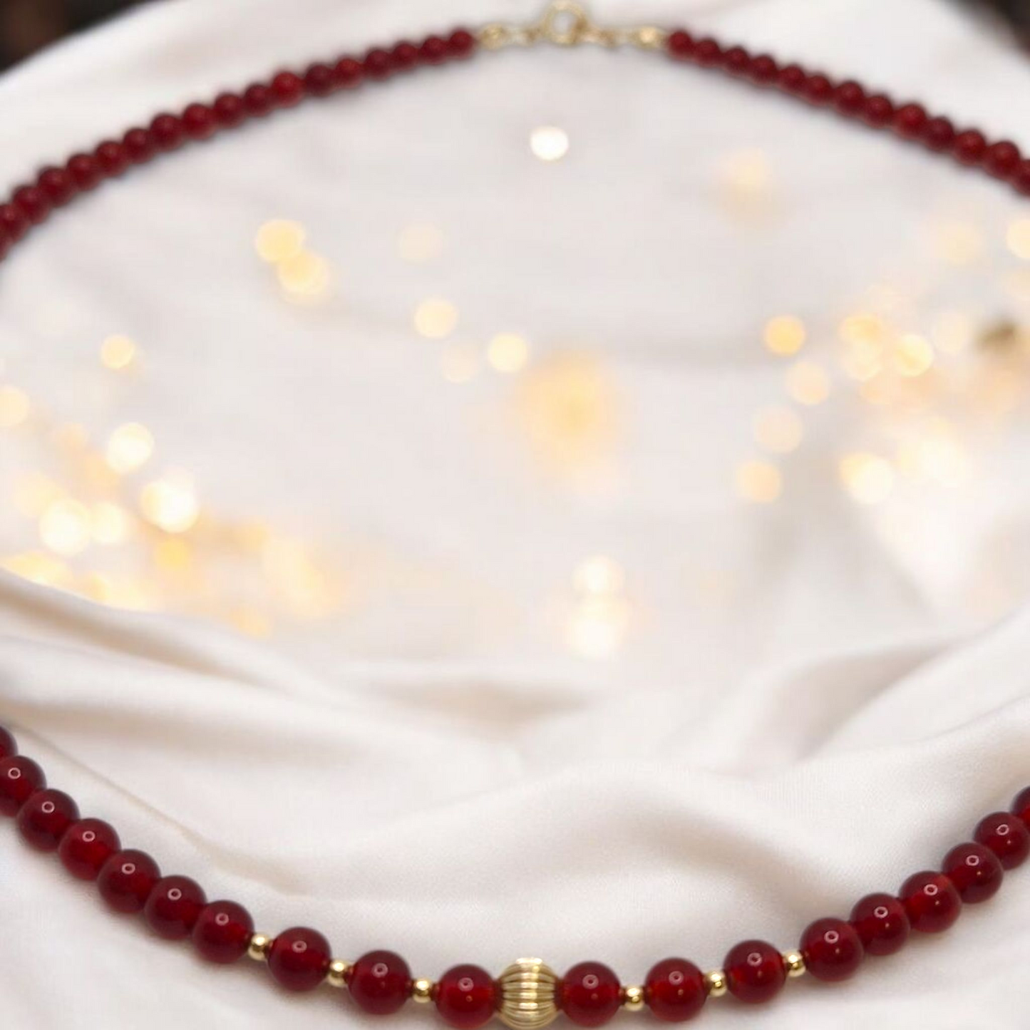 Red beaded necklace with gold accents on a white fabric background