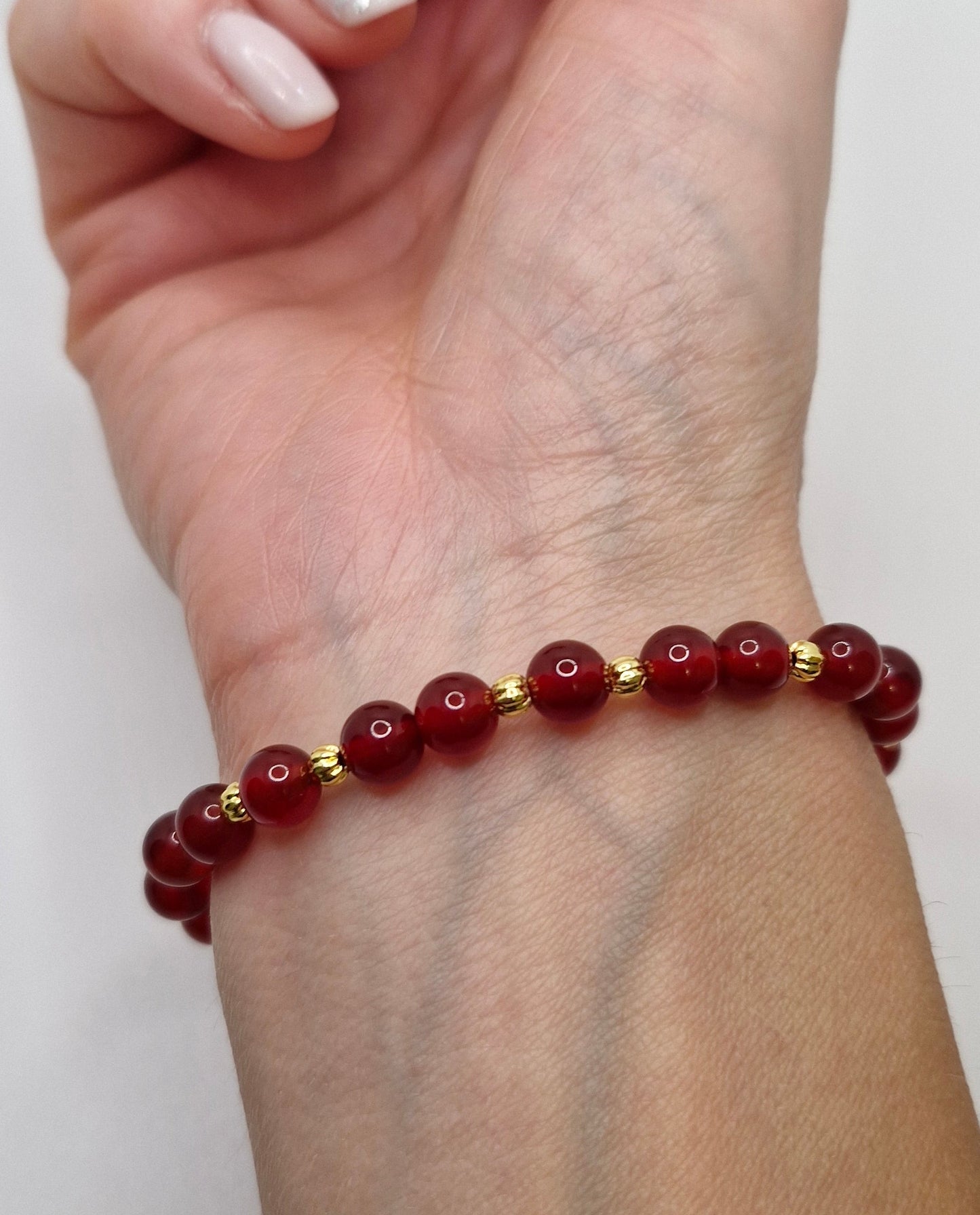 Hand wearing a red beaded bracelet on a plain background