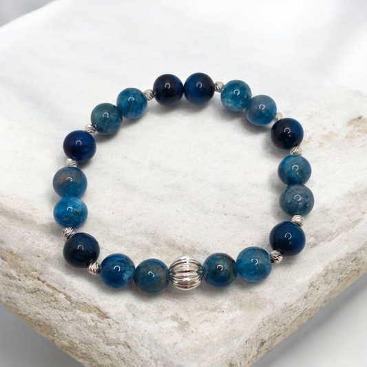 Blue beaded bracelet with a silver clasp on a white stone surface