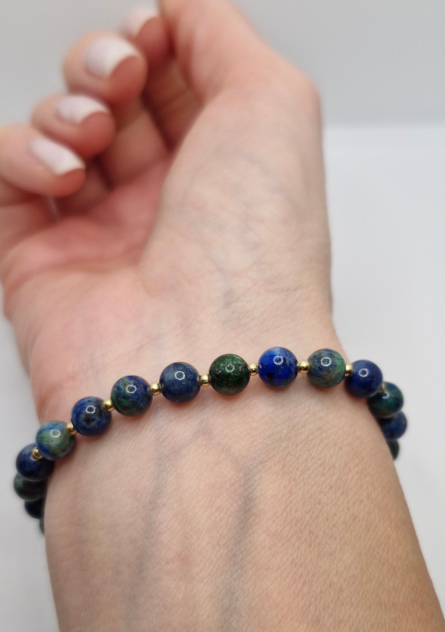 Hand wearing a bracelet with blue and green beads on a white background