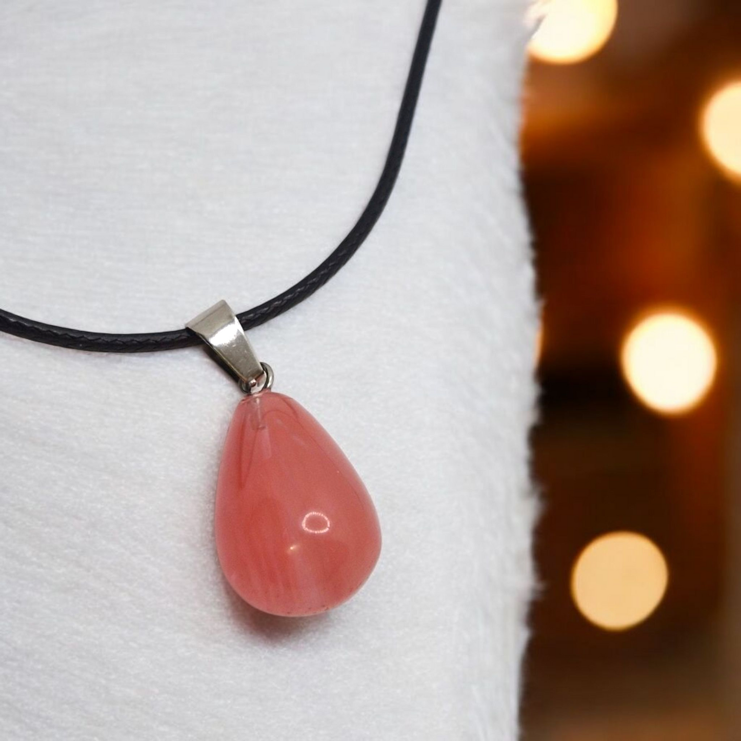 Close-up of natural Cherry Quartz 14x24mm teardrop pendant with black cord, polished finish and soft pink hue.