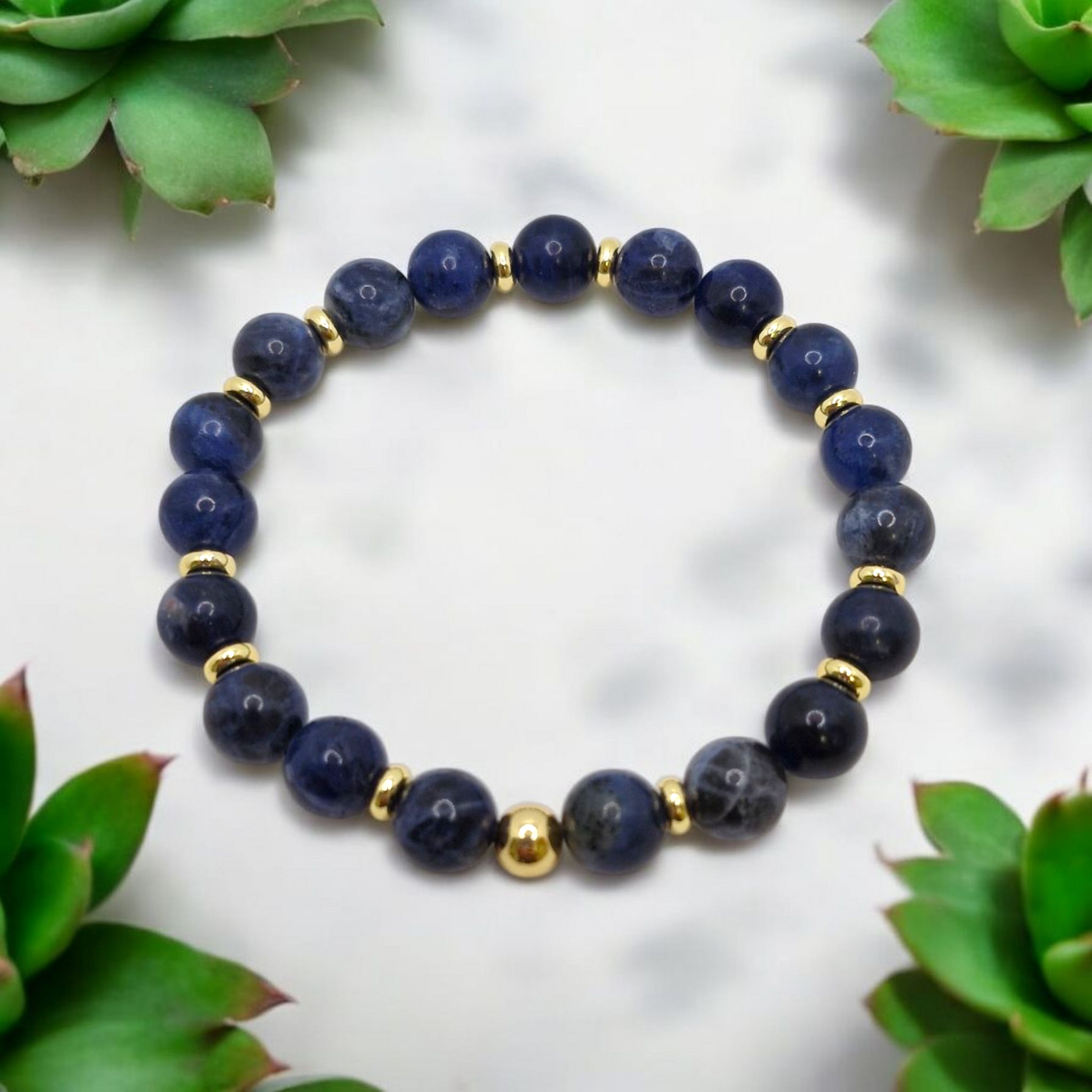 Navy blue beaded bracelet with gold accents on a white background with green plants.