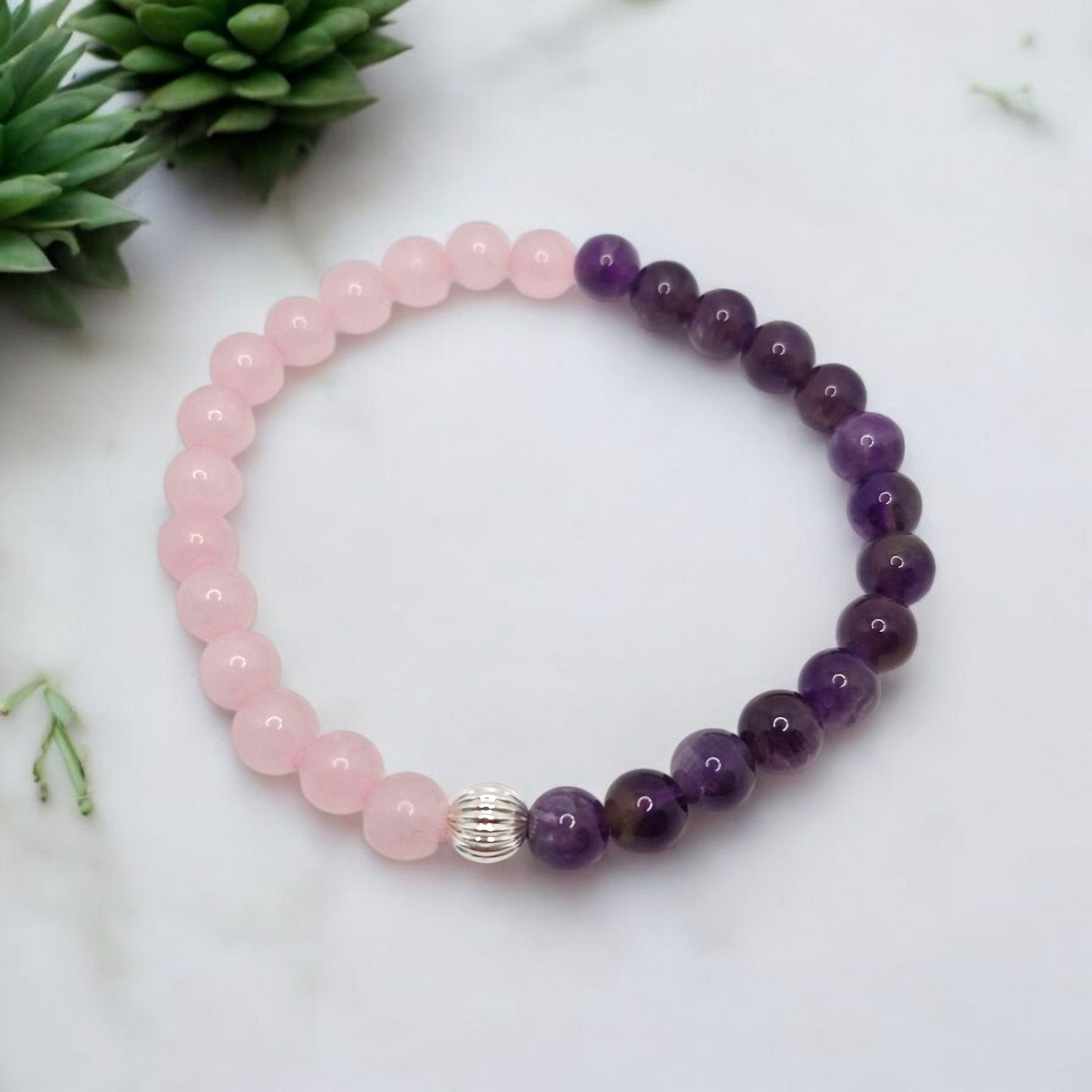 Beaded bracelet with pink and purple beads on a white surface with greenery.