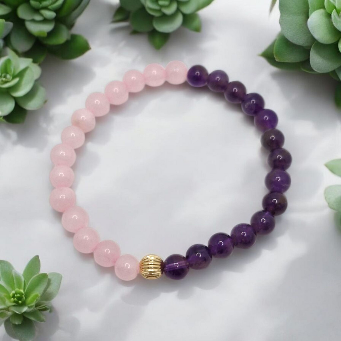 Beaded bracelet with pink and purple beads on a white surface with green plants.