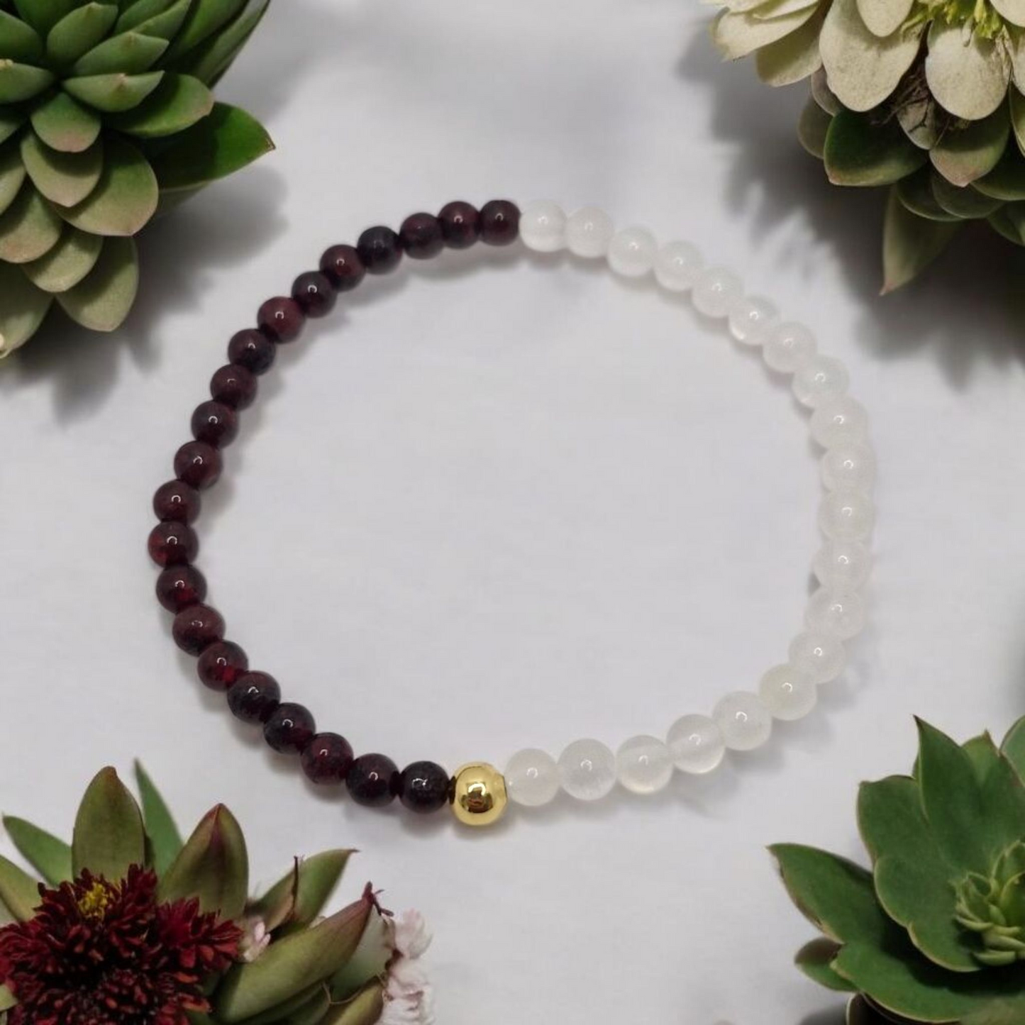 Beaded bracelet with maroon and white beads on a light surface with succulents around
