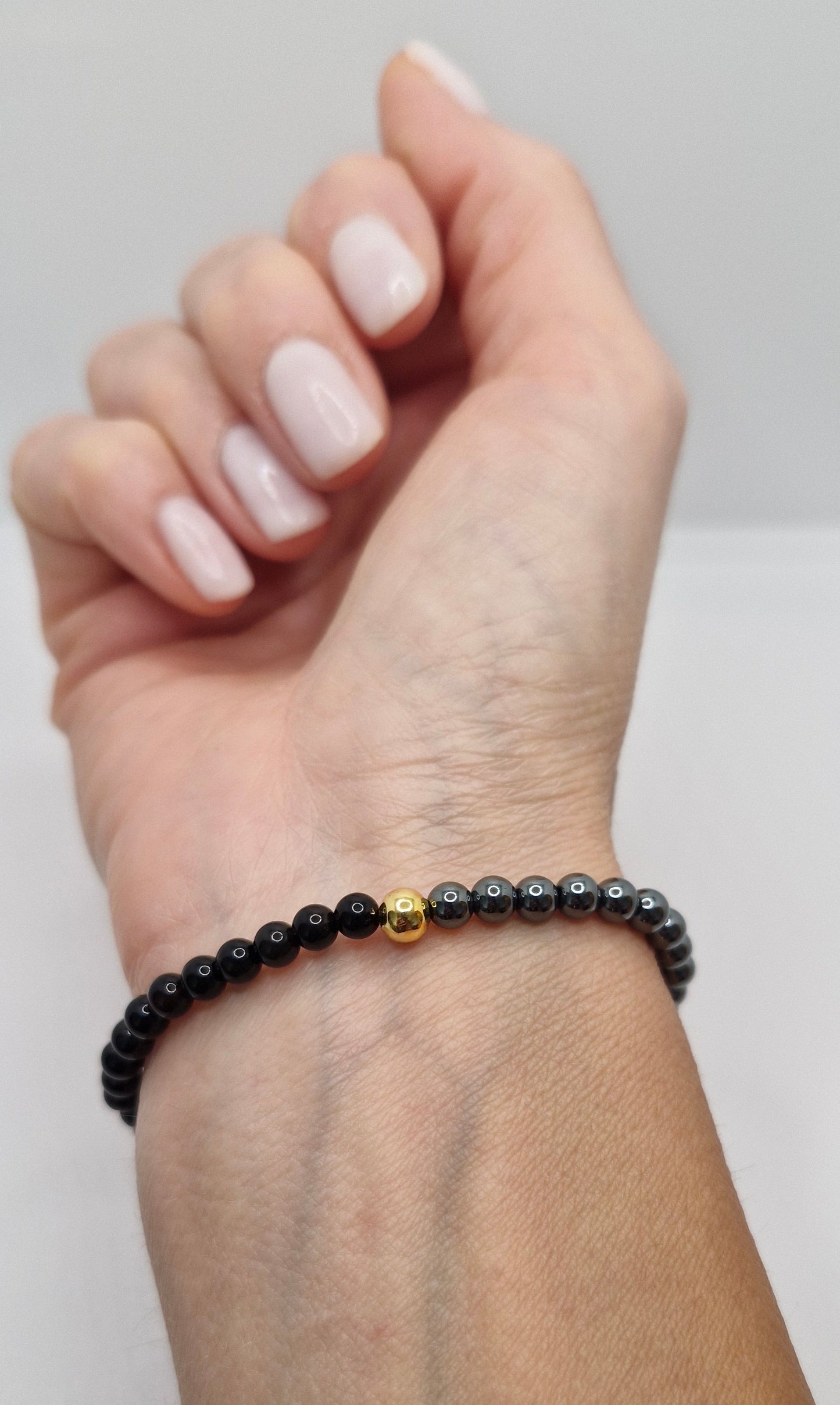 Hand wearing a black beaded bracelet on a plain background