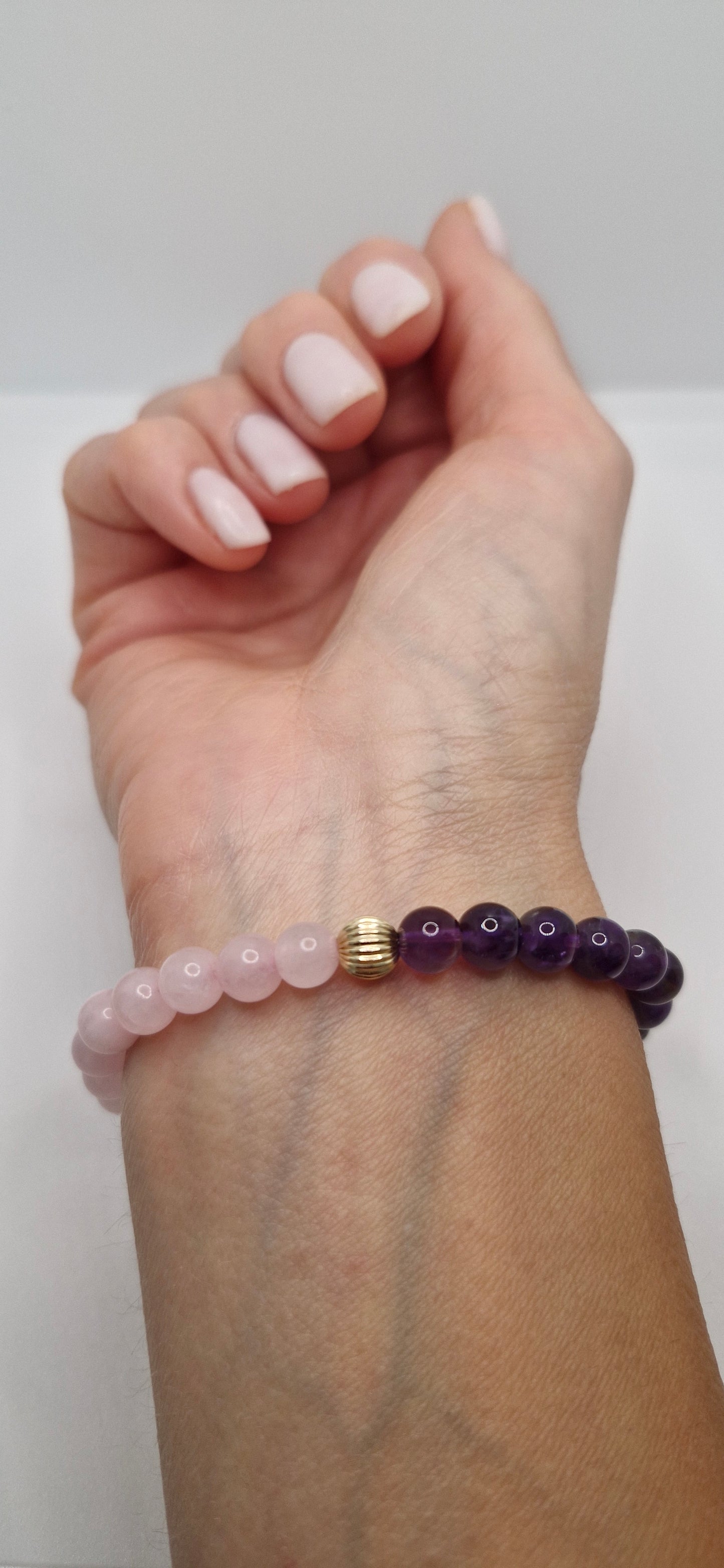 Hand wearing a bracelet with purple beads on a plain background