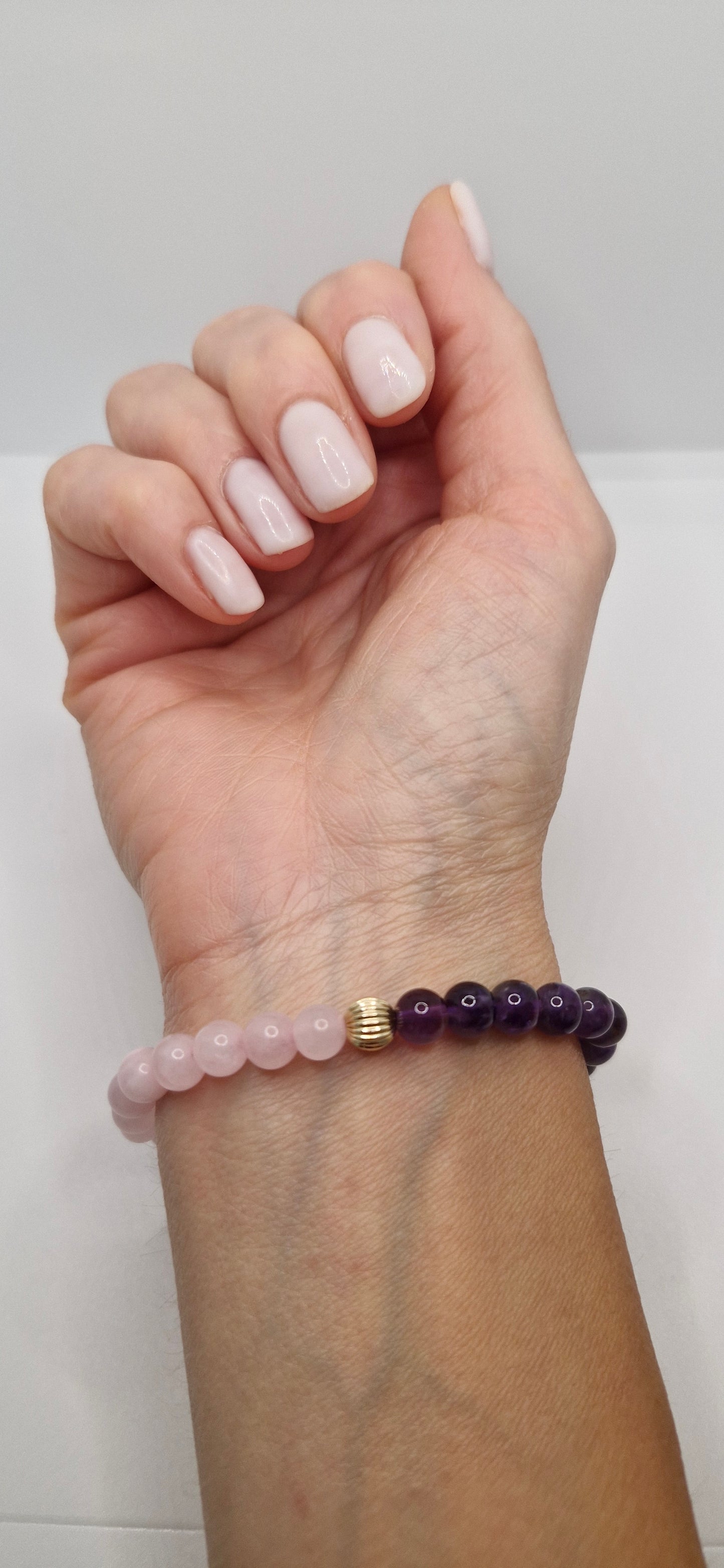 Hand wearing a bracelet with pink beads on a plain background