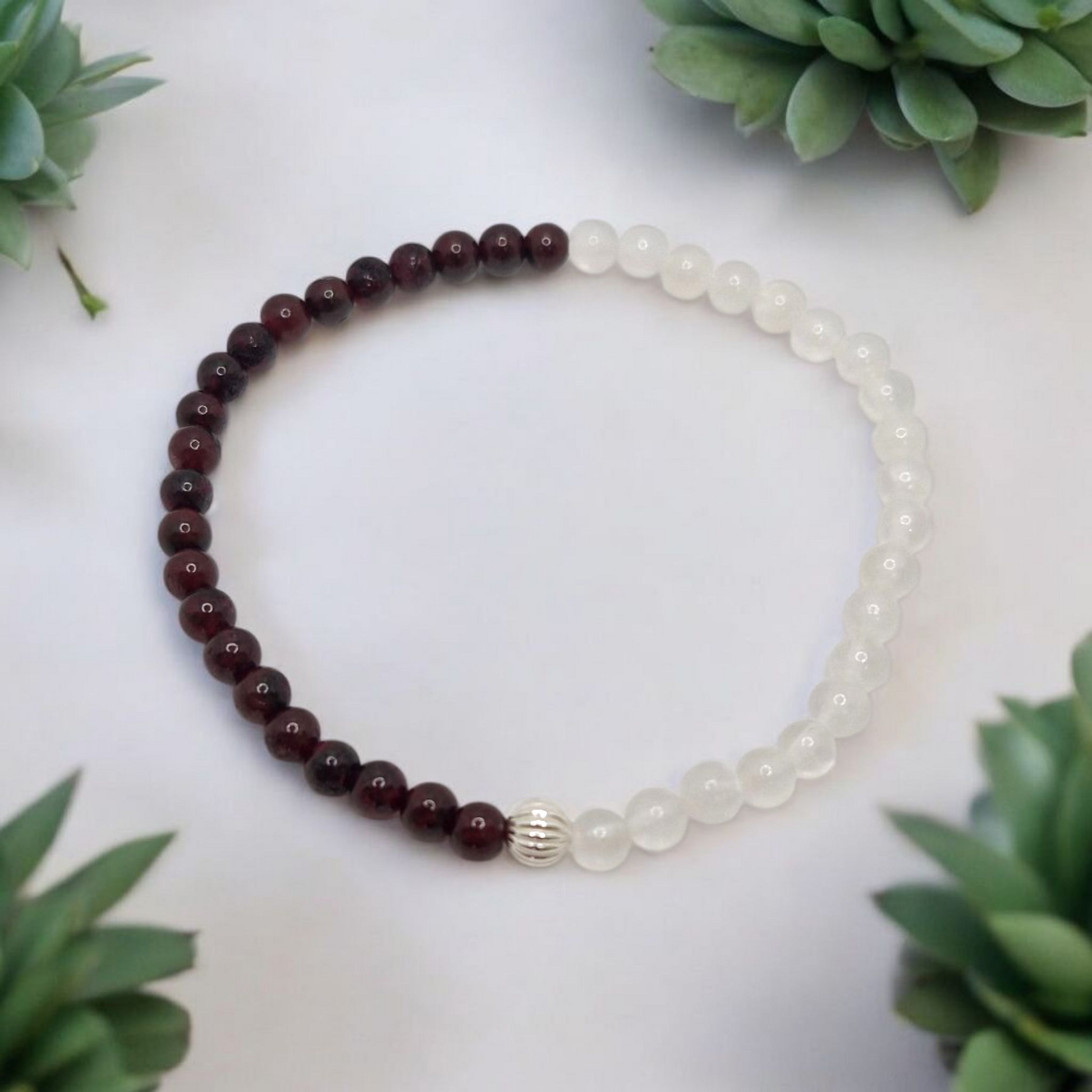 Bracelet with red and white beads on a white surface with green plants around