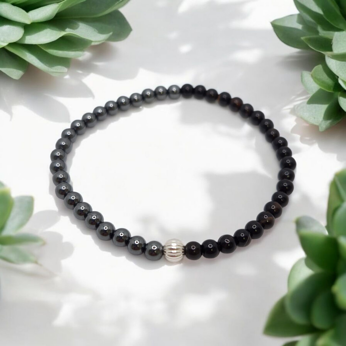 Black beaded bracelet with a silver accent on a white surface with green plants around