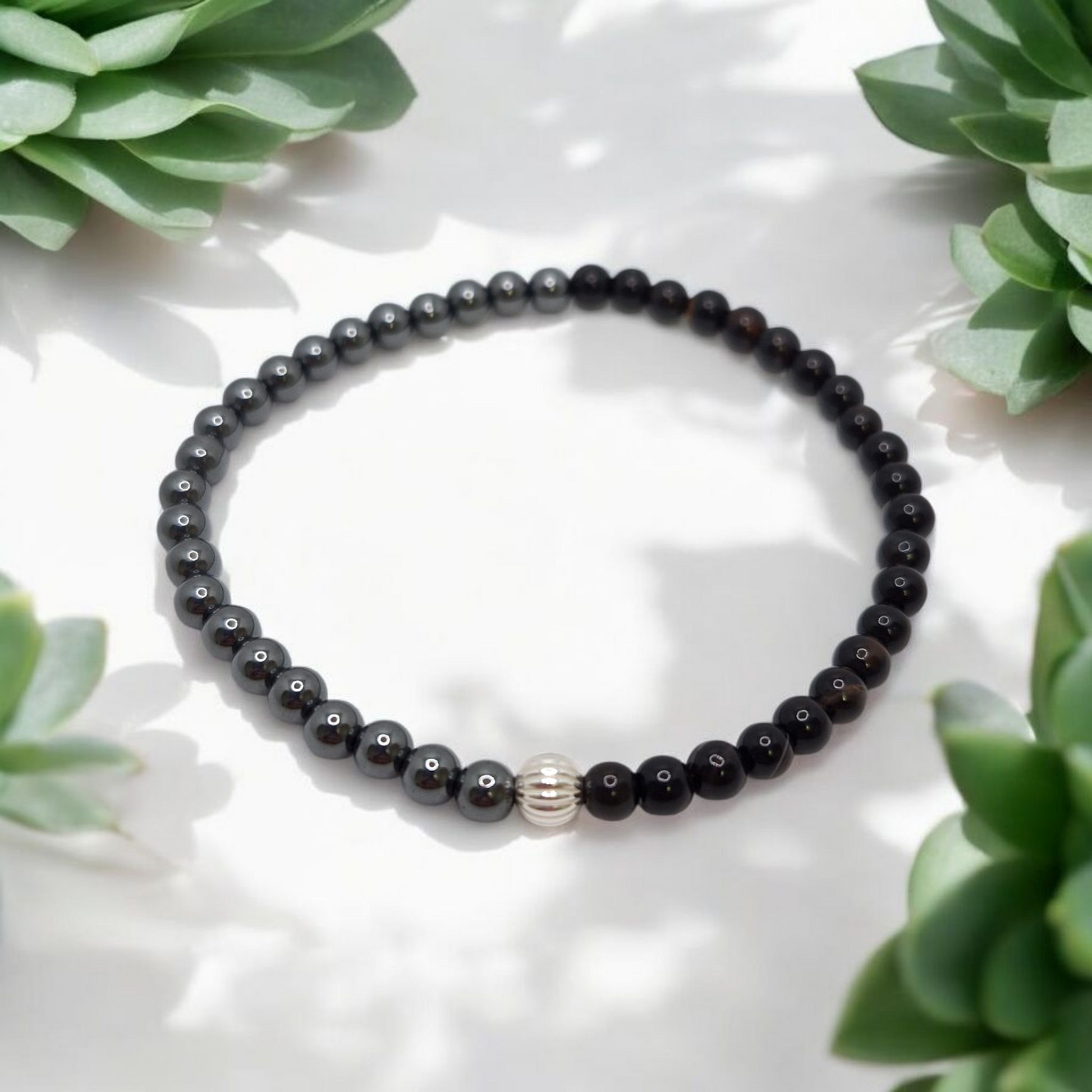 Black beaded bracelet with a silver accent on a white surface with green plants around