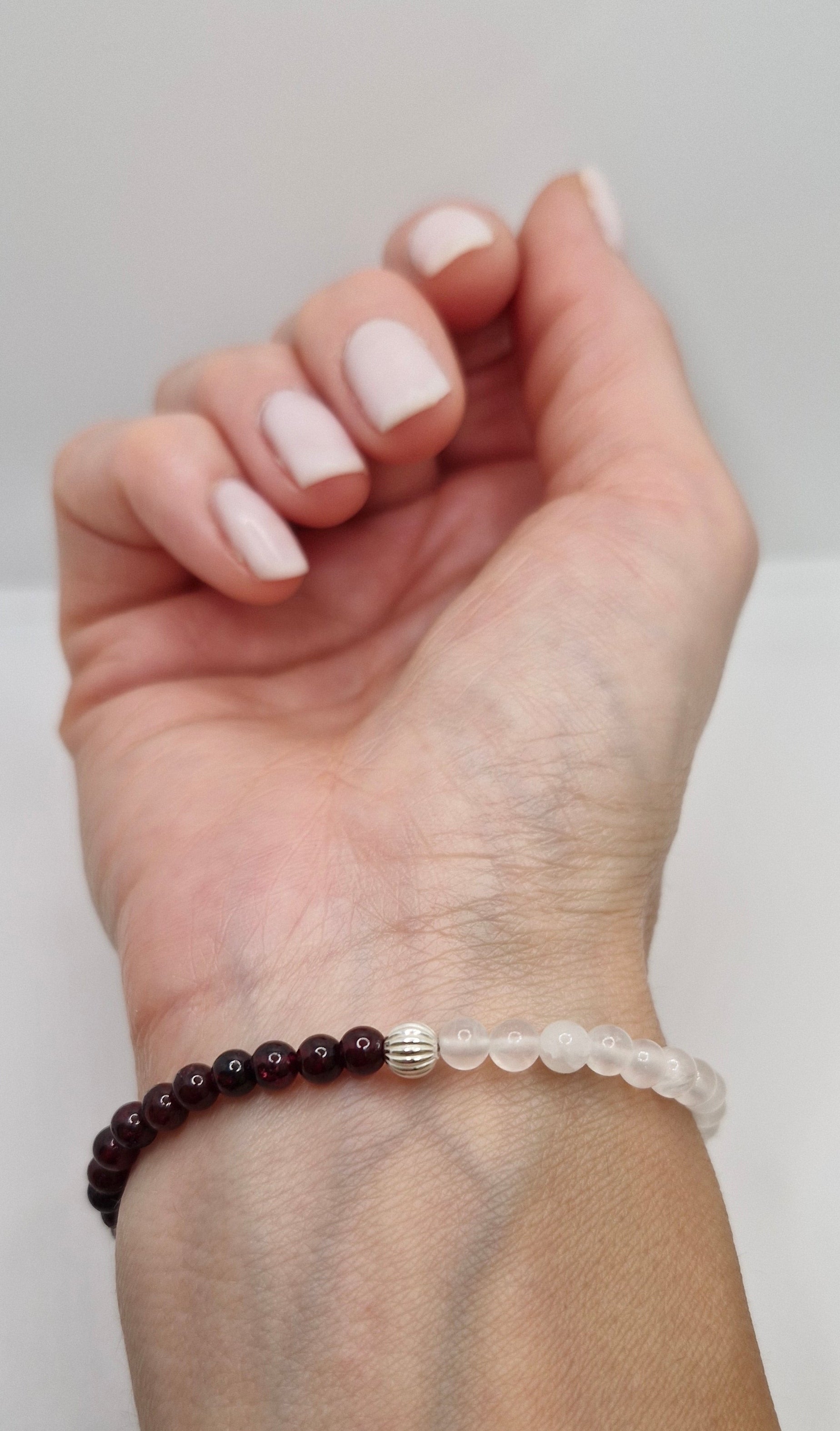 Hand wearing a bracelet with dark beads on a plain background