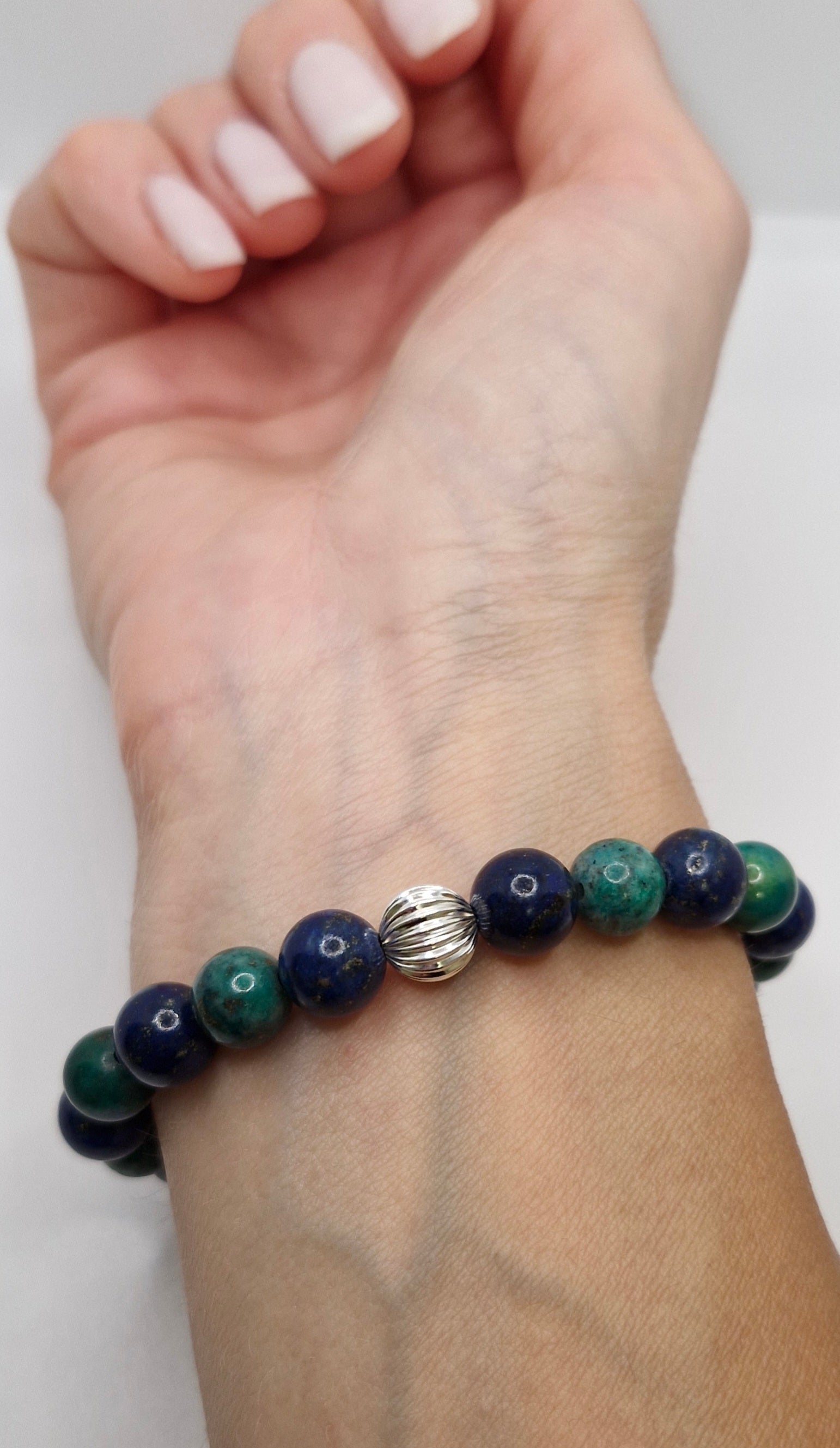 Hand wearing a bracelet with blue and green beads on a white background