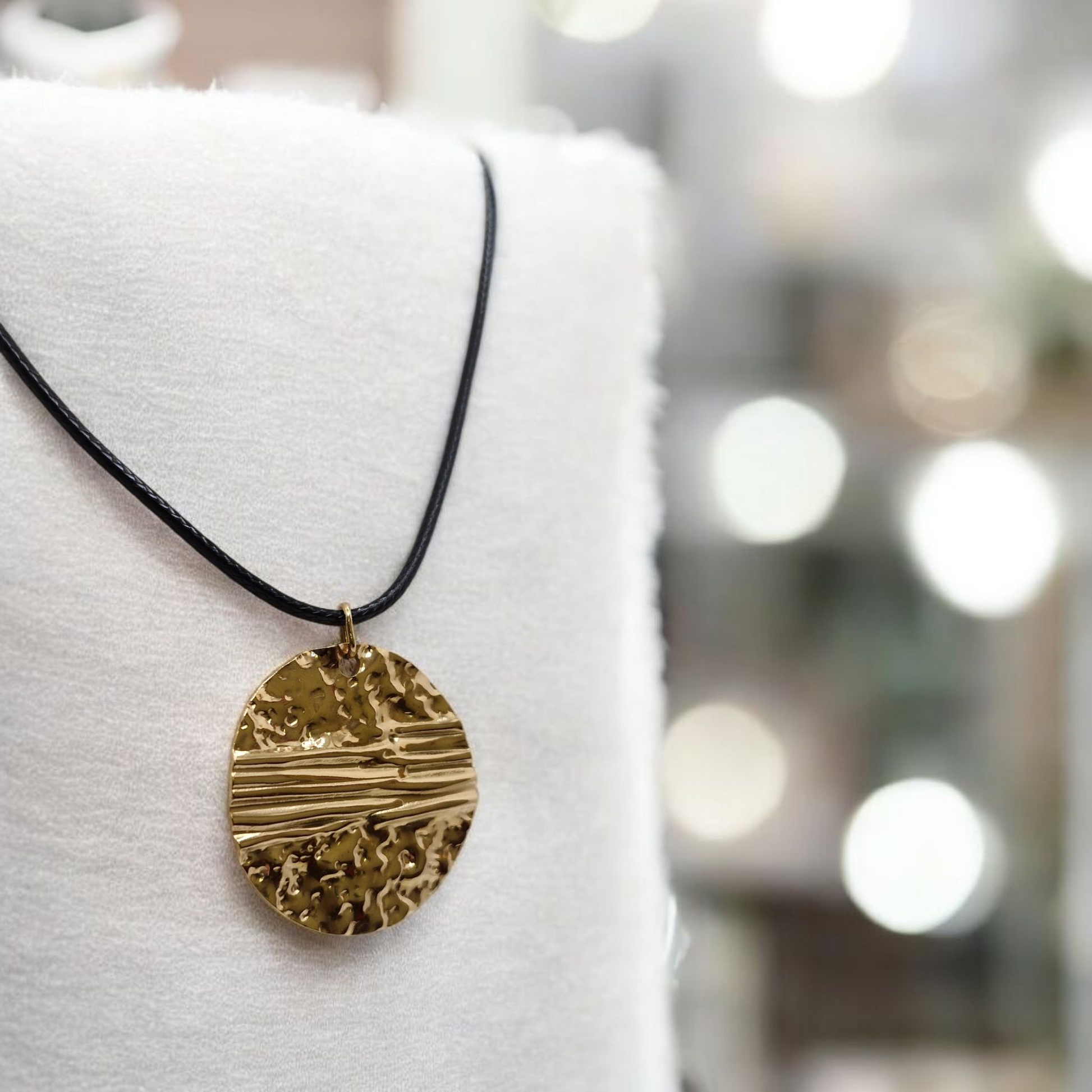 Gold necklace with a textured pendant on a mannequin against a blurred background