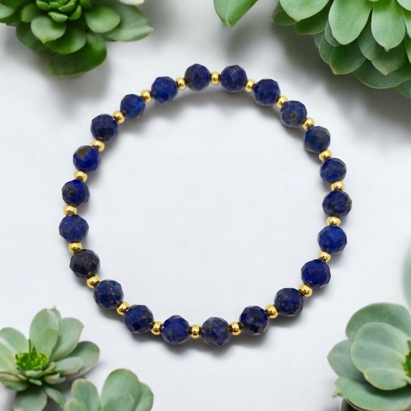 Lapis lazuli beaded bracelet with gold accents on a white background with succulents