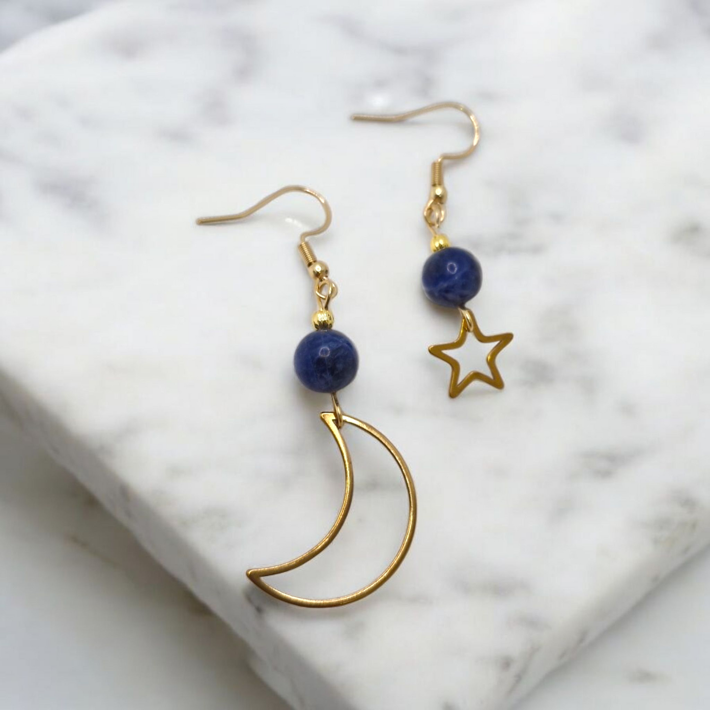 Gold earrings with blue beads and star/moon designs on a marble surface