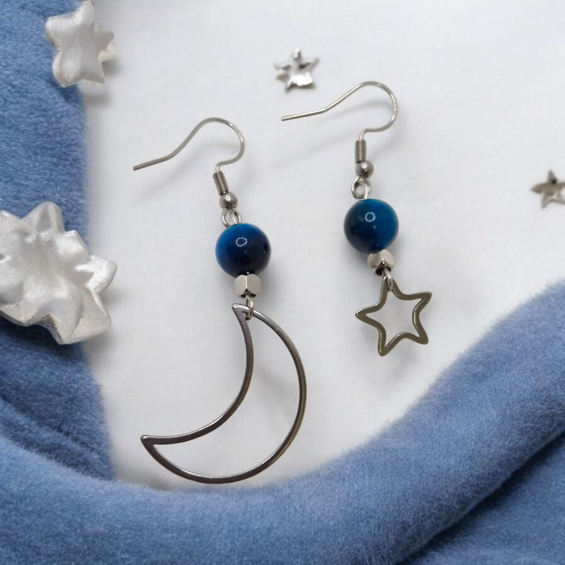 Pair of earrings with moon and star designs on a blue fabric background