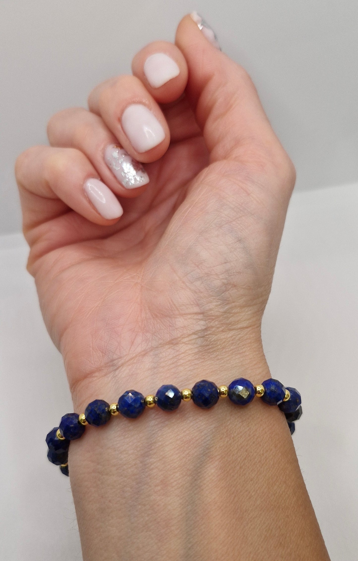 Hand wearing a blue beaded bracelet with gold accents on a plain background