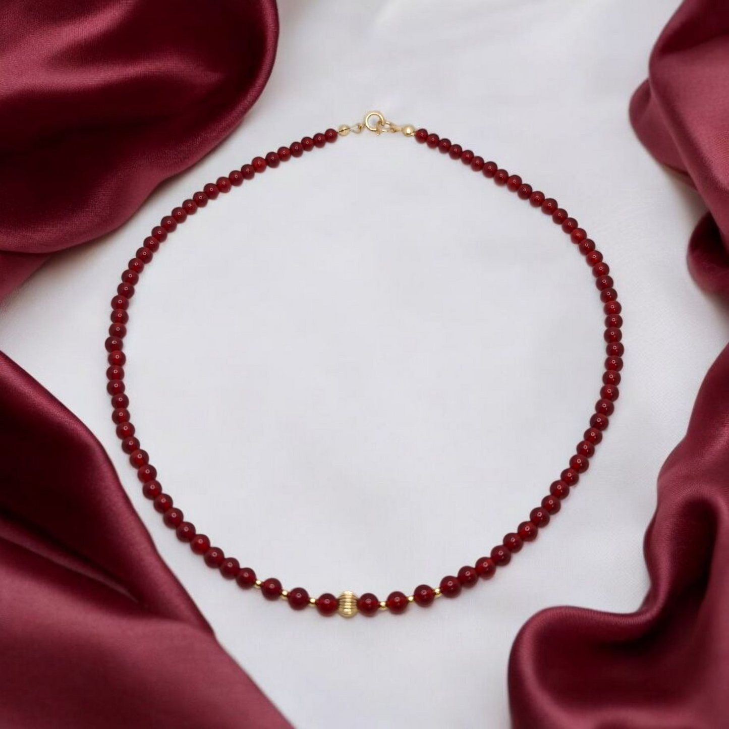 Red beaded necklace with a gold clasp on a white background with red satin fabric