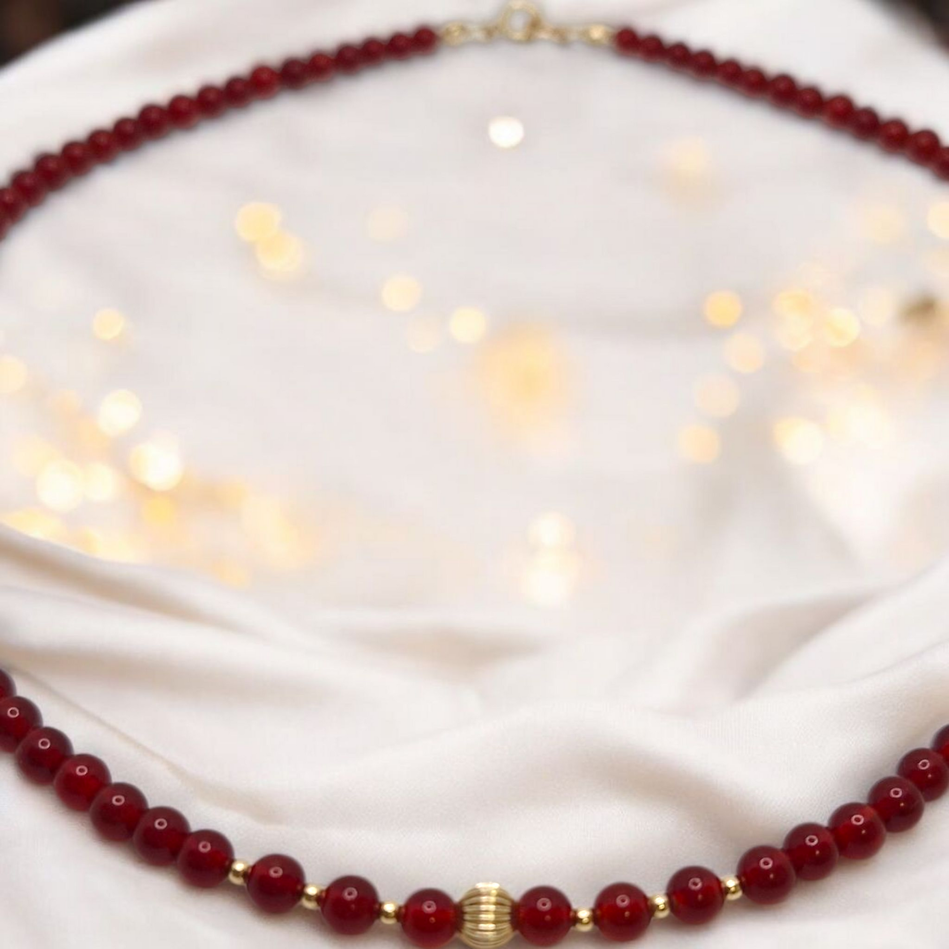 Red beaded necklace with gold accents on a white fabric background