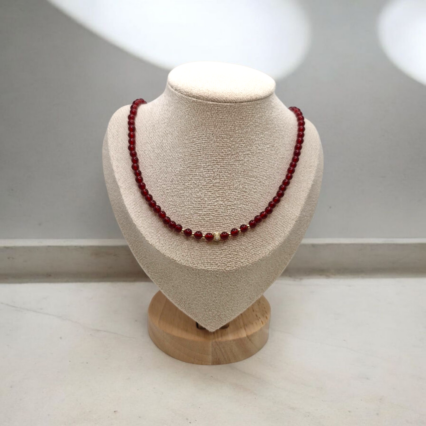 Red beaded necklace on a mannequin bust with a plain background