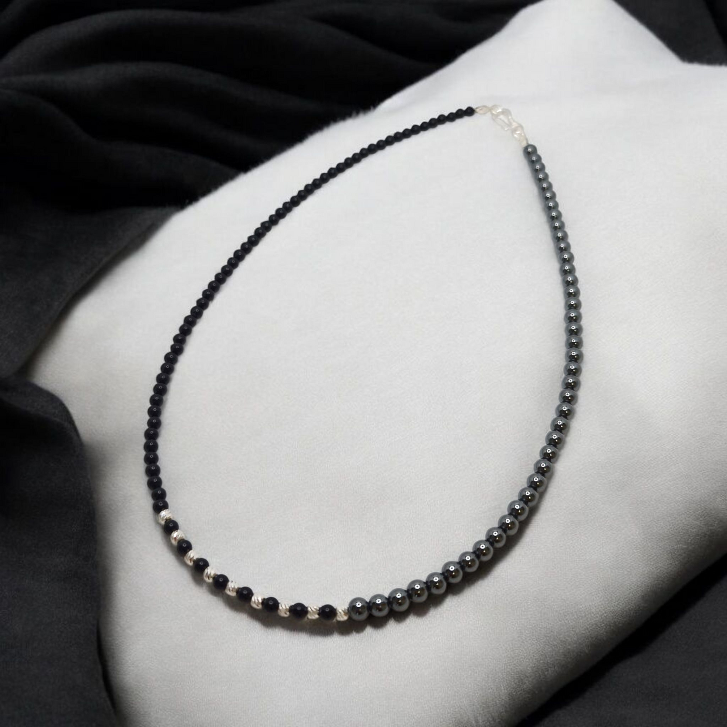 Black beaded necklace on a person's arm against a dark background