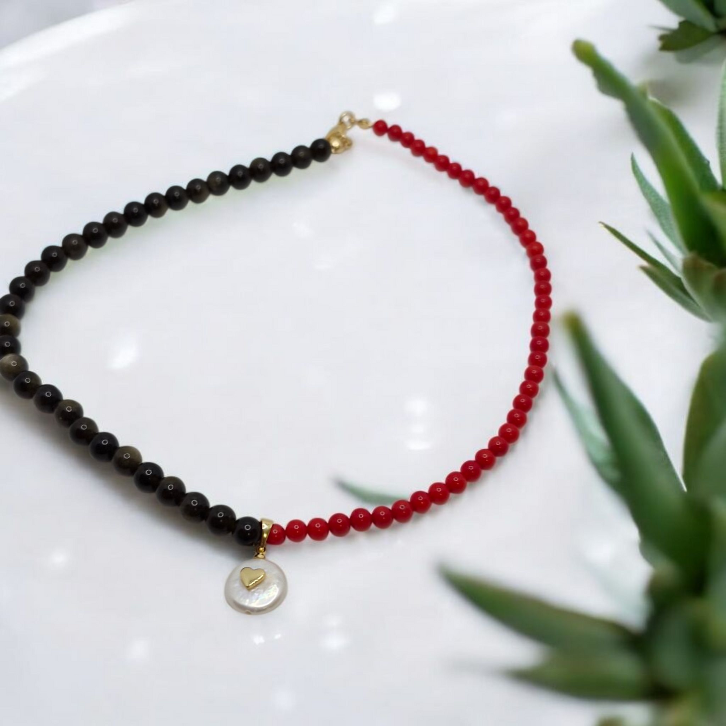Necklace with black and red beads on a white surface with greenery