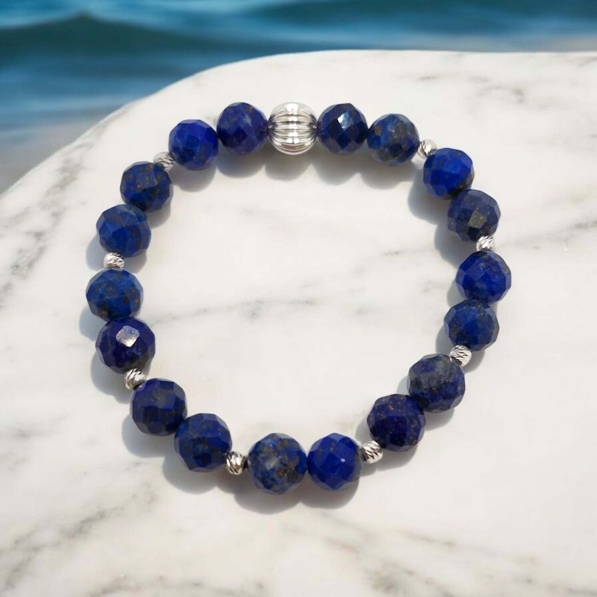 Blue beaded bracelet with silver accents on a marble surface with a blue background