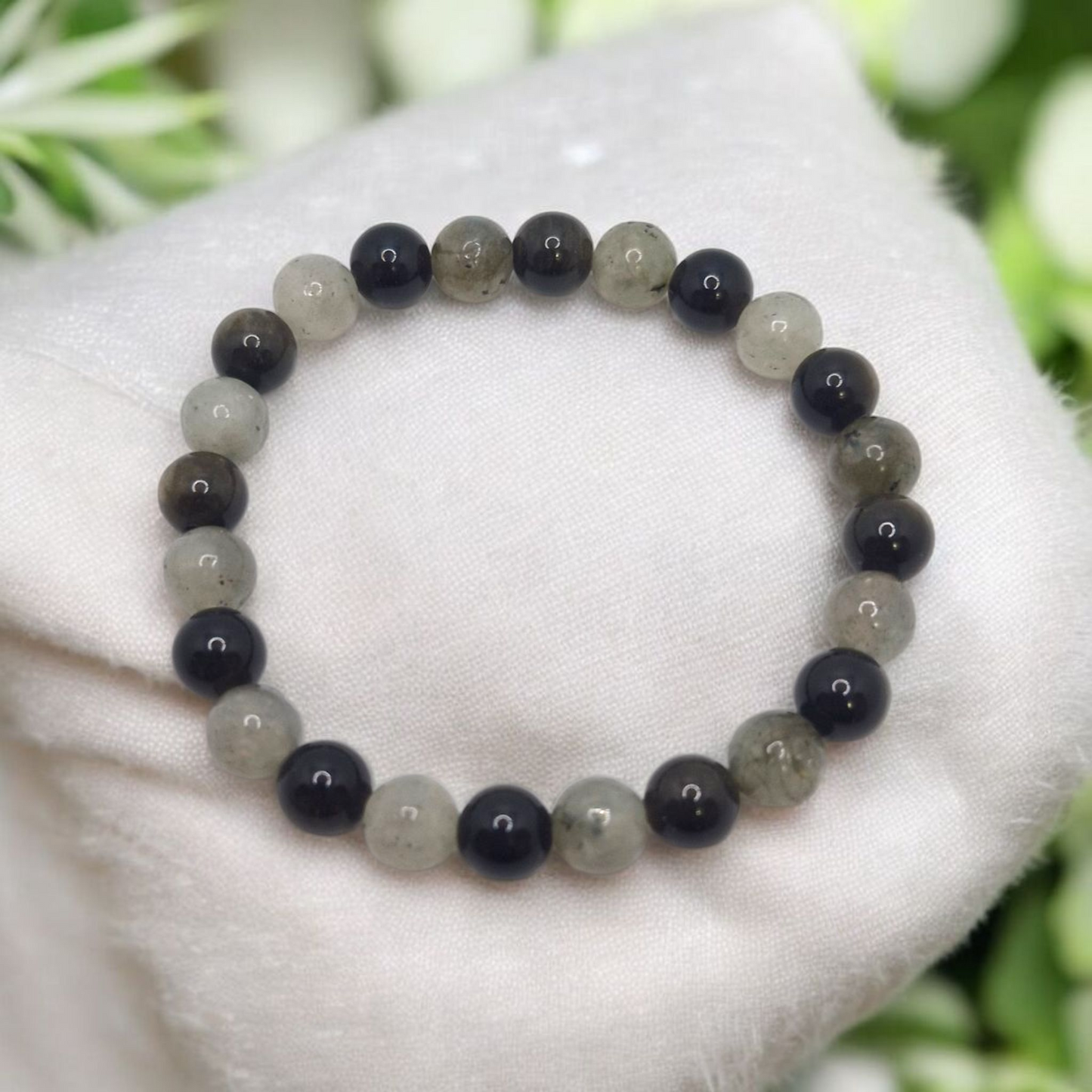 Beaded bracelet with black and gray beads on a white surface with greenery in the background