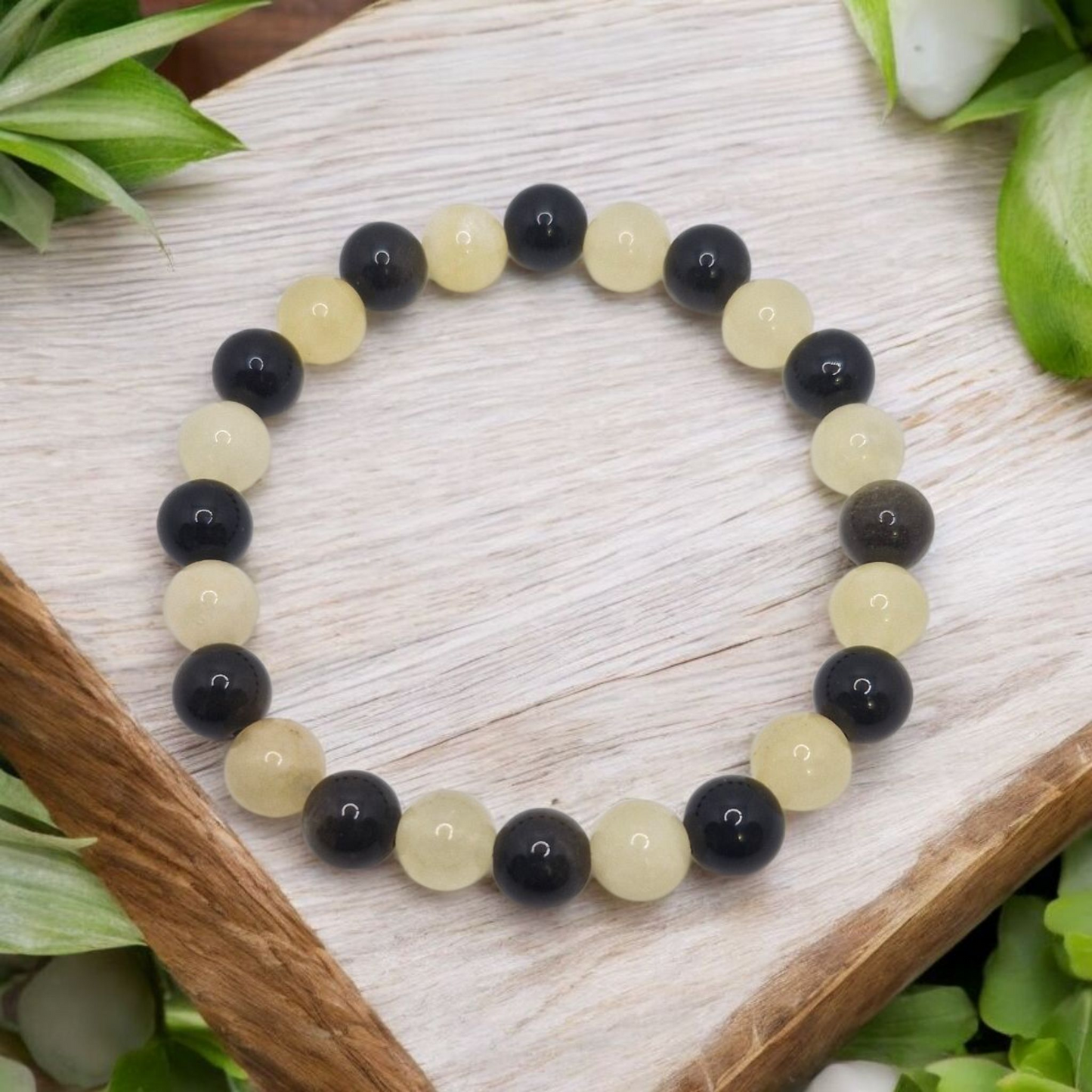 Beaded bracelet with black and yellow beads on a wooden surface with green leaves.