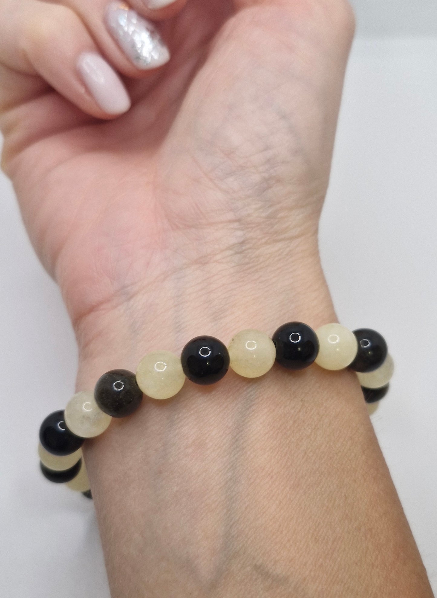 Beaded bracelet with black and beige beads on a wrist against a white background