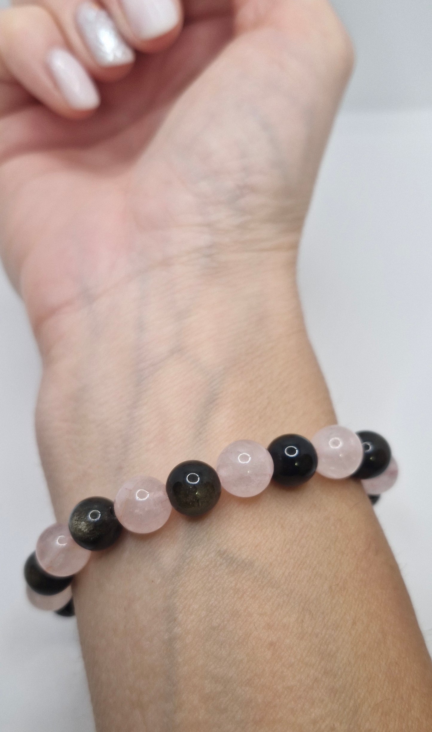 Bracelet with black and rose quartz beads on a wrist against a white background