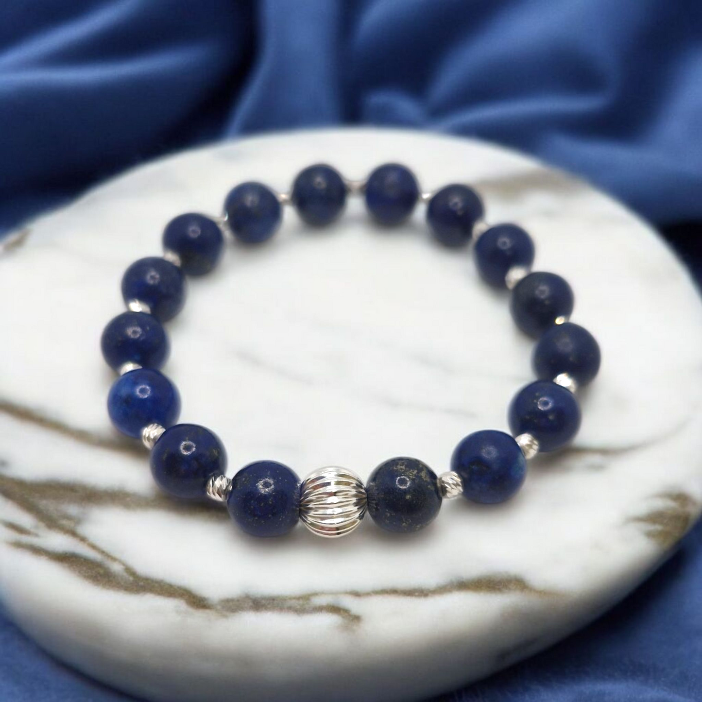 Navy blue beaded bracelet with silver accents on a marble surface with blue fabric background