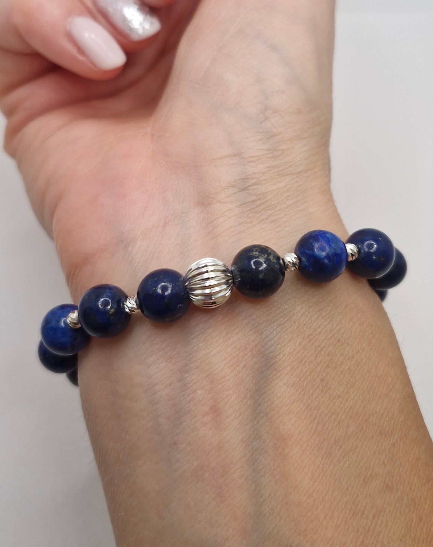 Beaded bracelet with blue beads and a silver clasp on a wrist against a white background