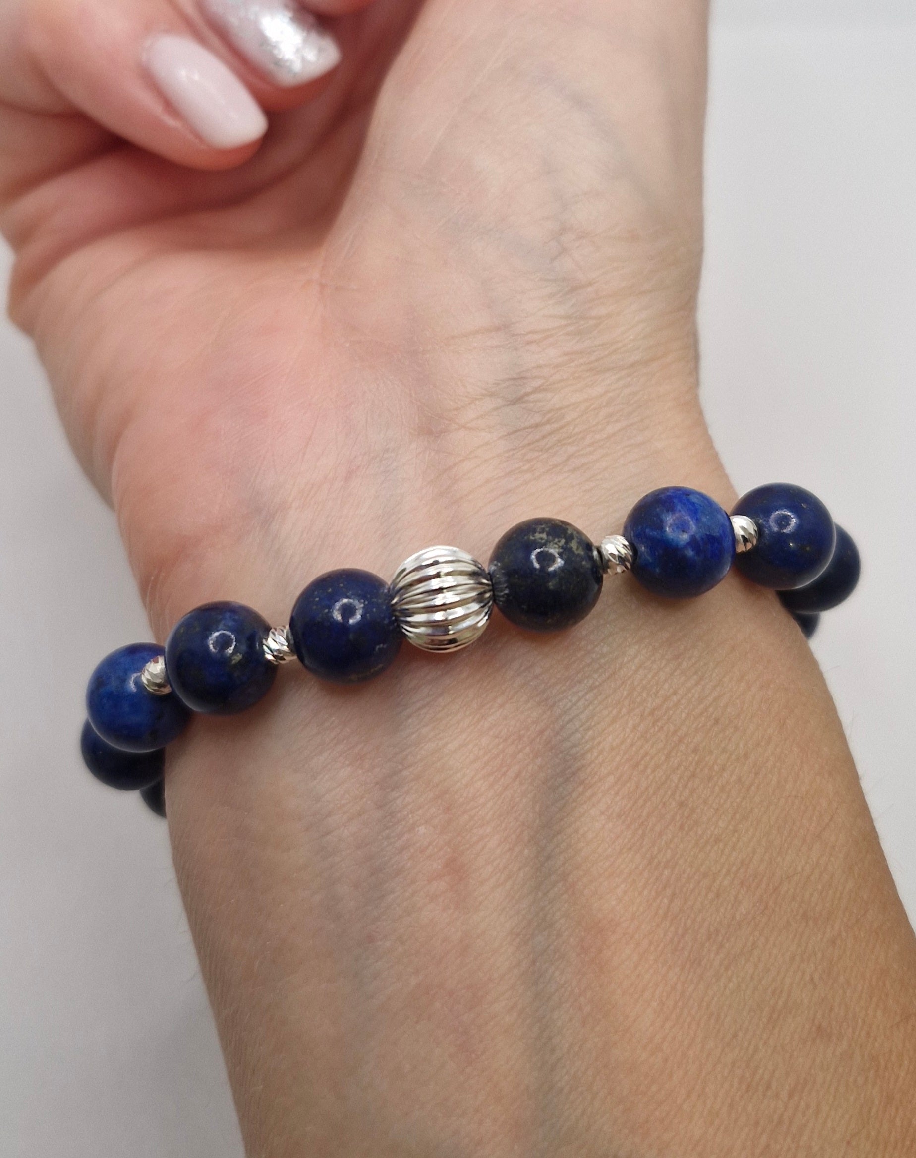 Beaded bracelet with blue beads and a silver clasp on a wrist against a white background