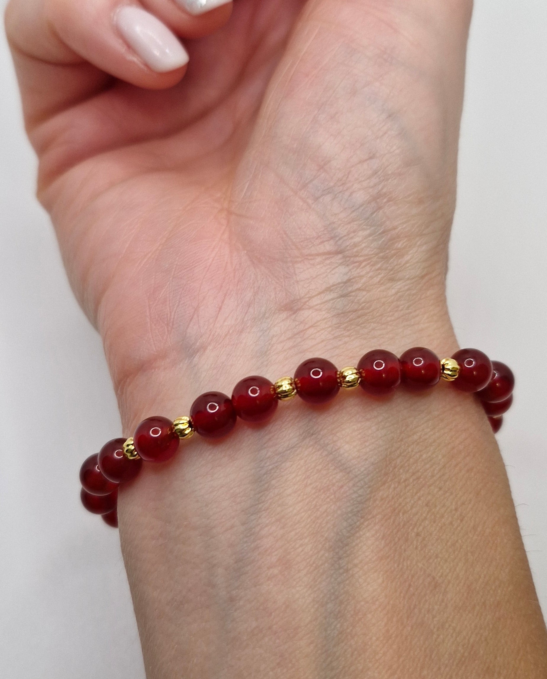 Hand wearing a red beaded bracelet on a plain background