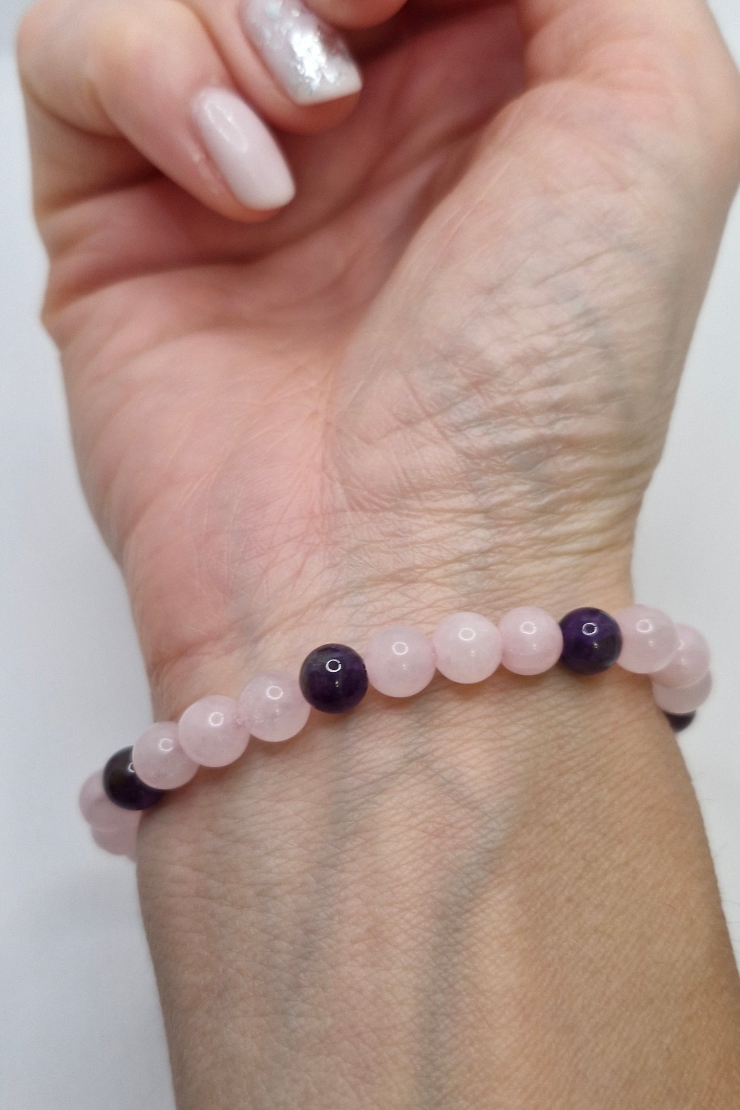 Hand wearing a bracelet with pink and purple beads on a white background