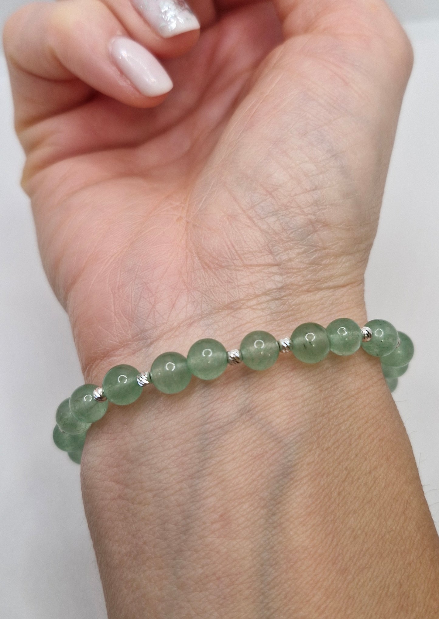 Green beaded bracelet on a wrist with a white background