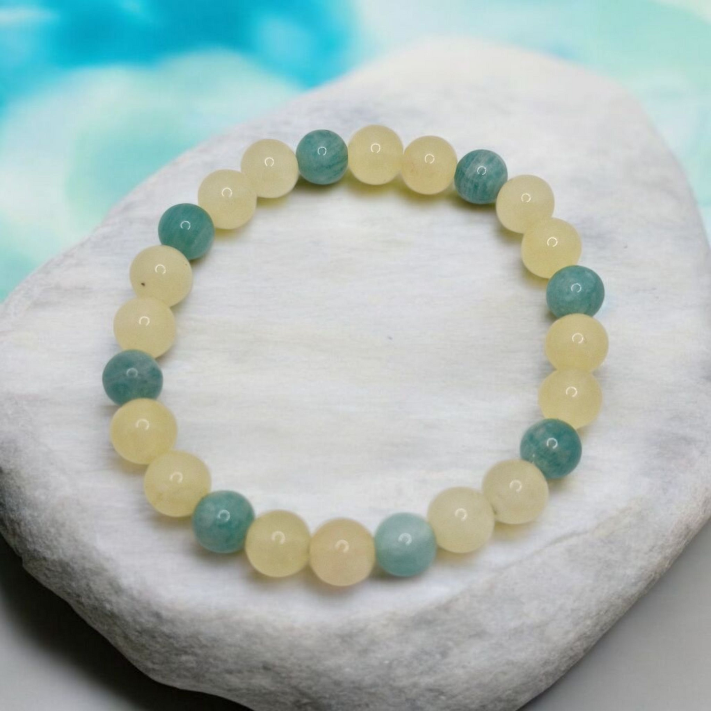 Beaded bracelet with green and yellow beads on a white stone with a blurred blue background