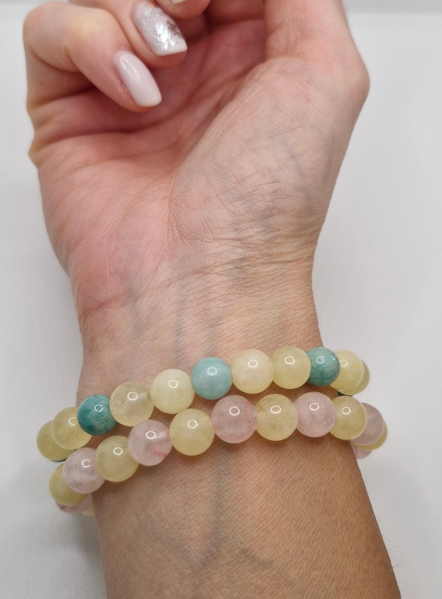 Hand wearing two beaded bracelets on a white background