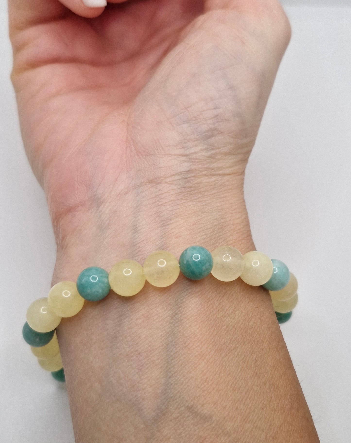 Hand wearing a bracelet with green and yellow beads on a white background