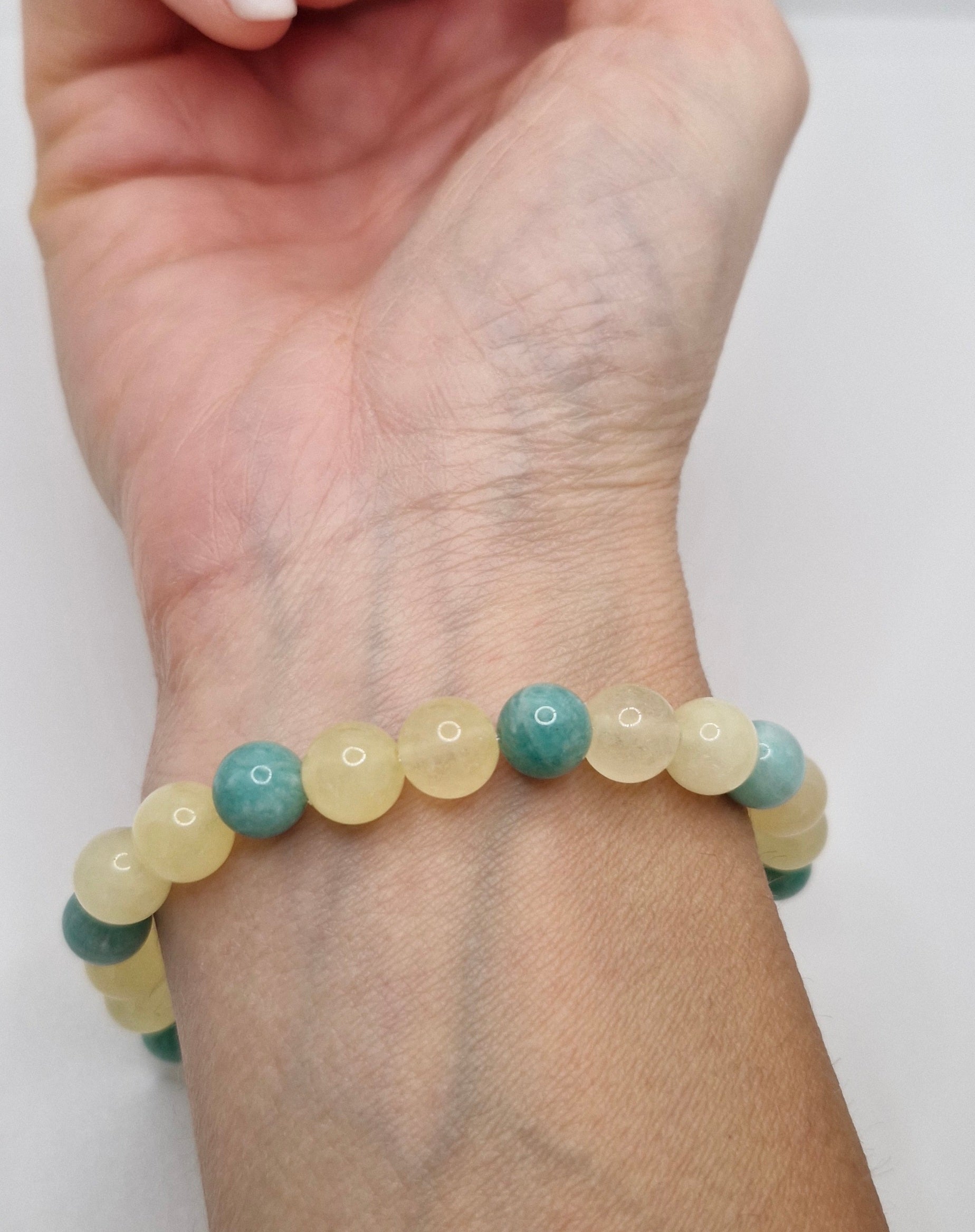 Hand wearing a bracelet with green and yellow beads on a white background