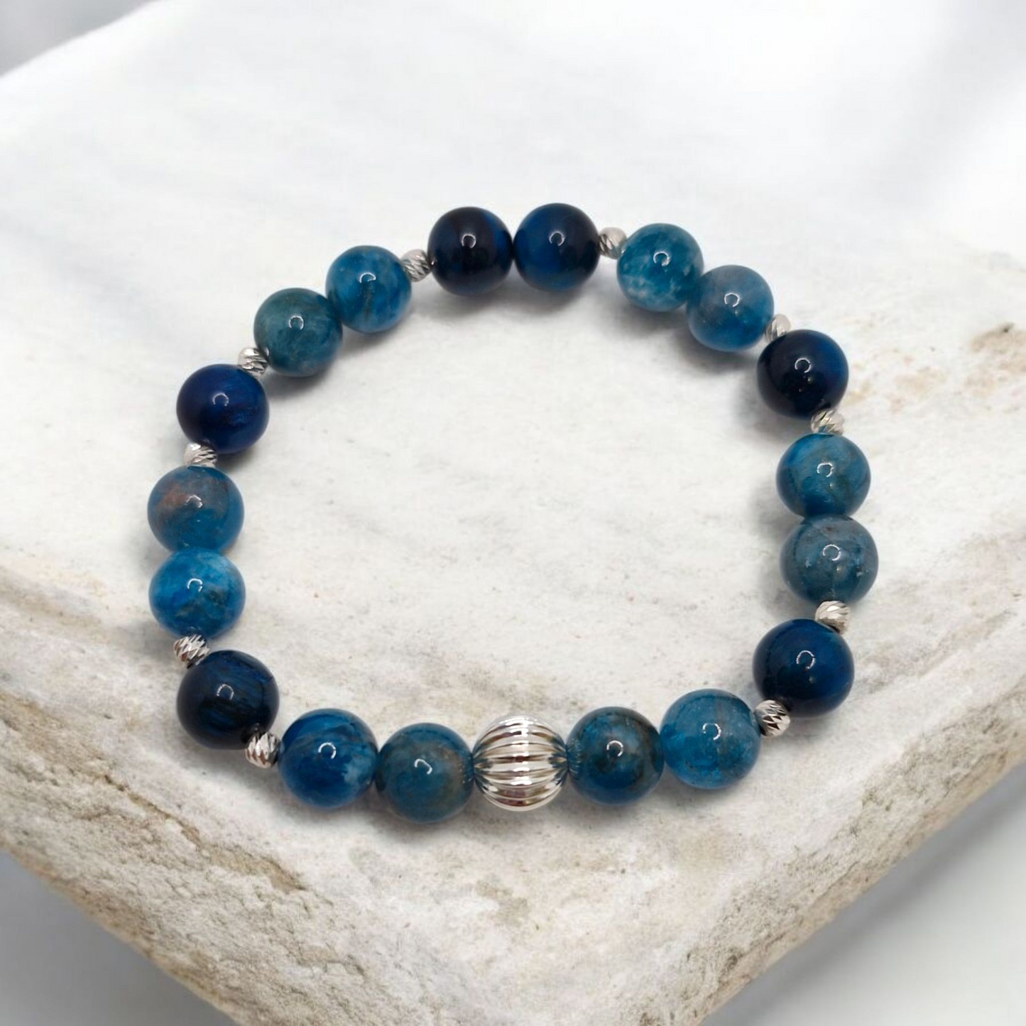 Blue beaded bracelet with a silver clasp on a white stone surface