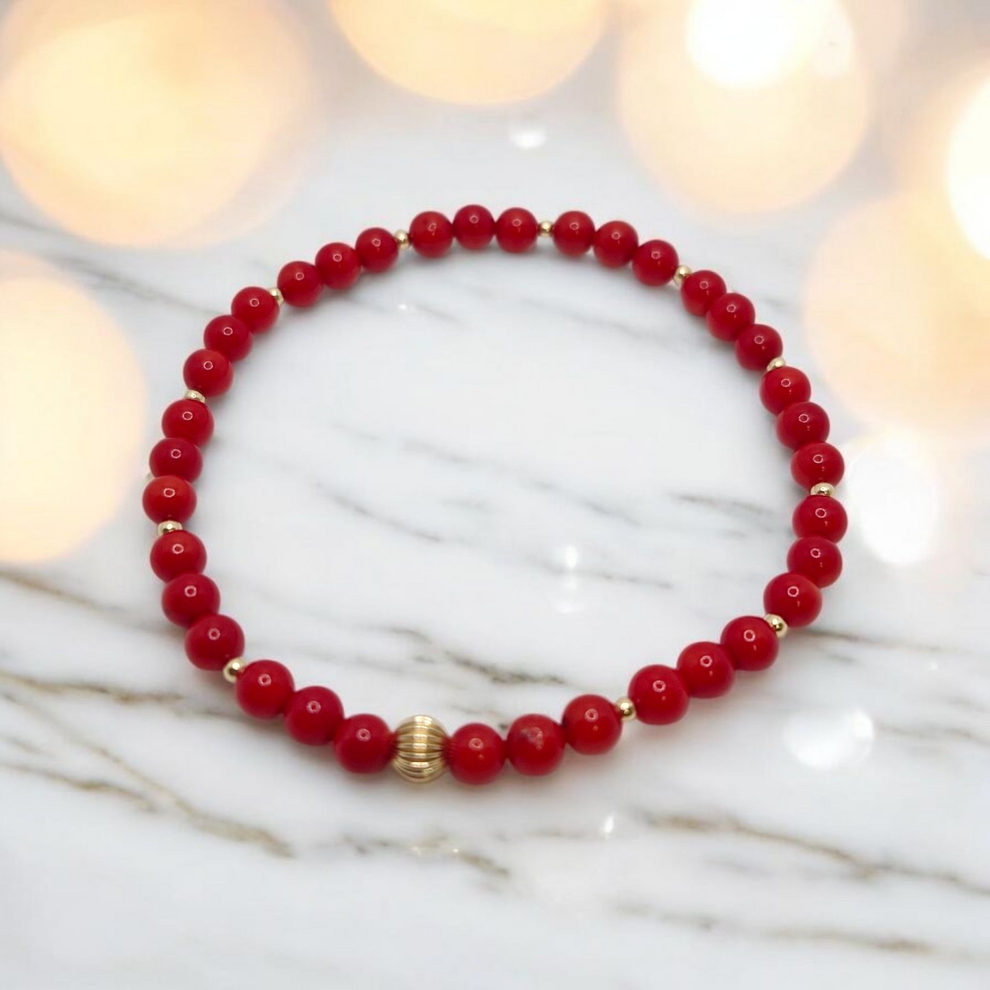 Red beaded bracelet with gold accents on a marble surface with blurred lights in the background