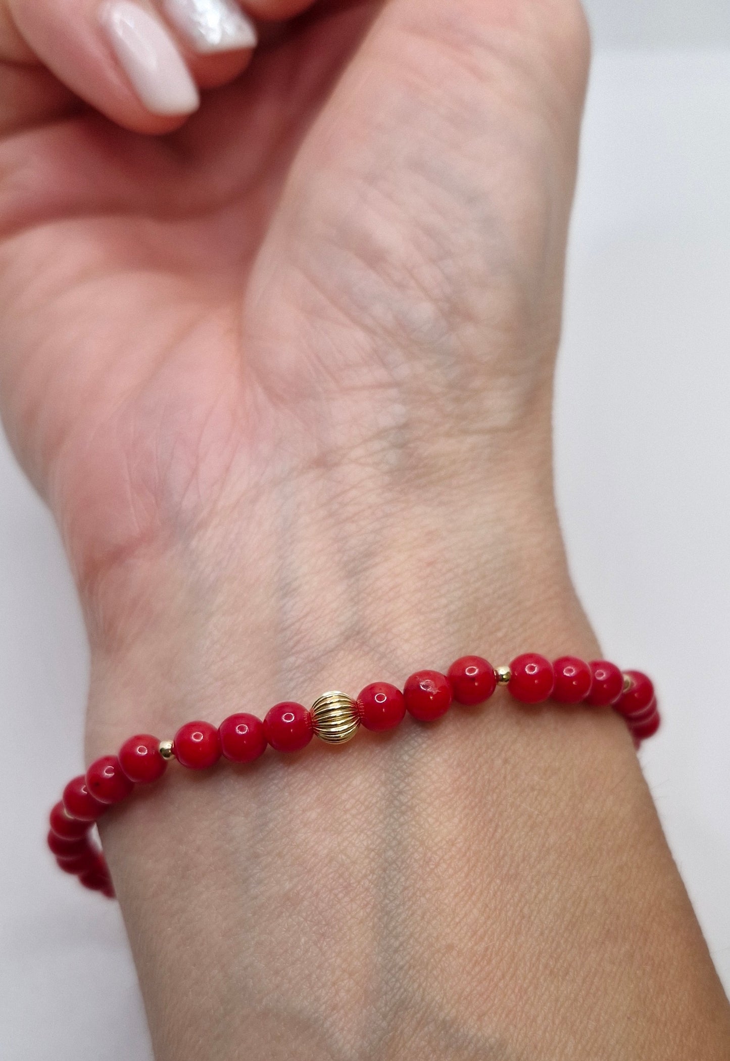 Red beaded bracelet with a gold clasp on a wrist against a white background