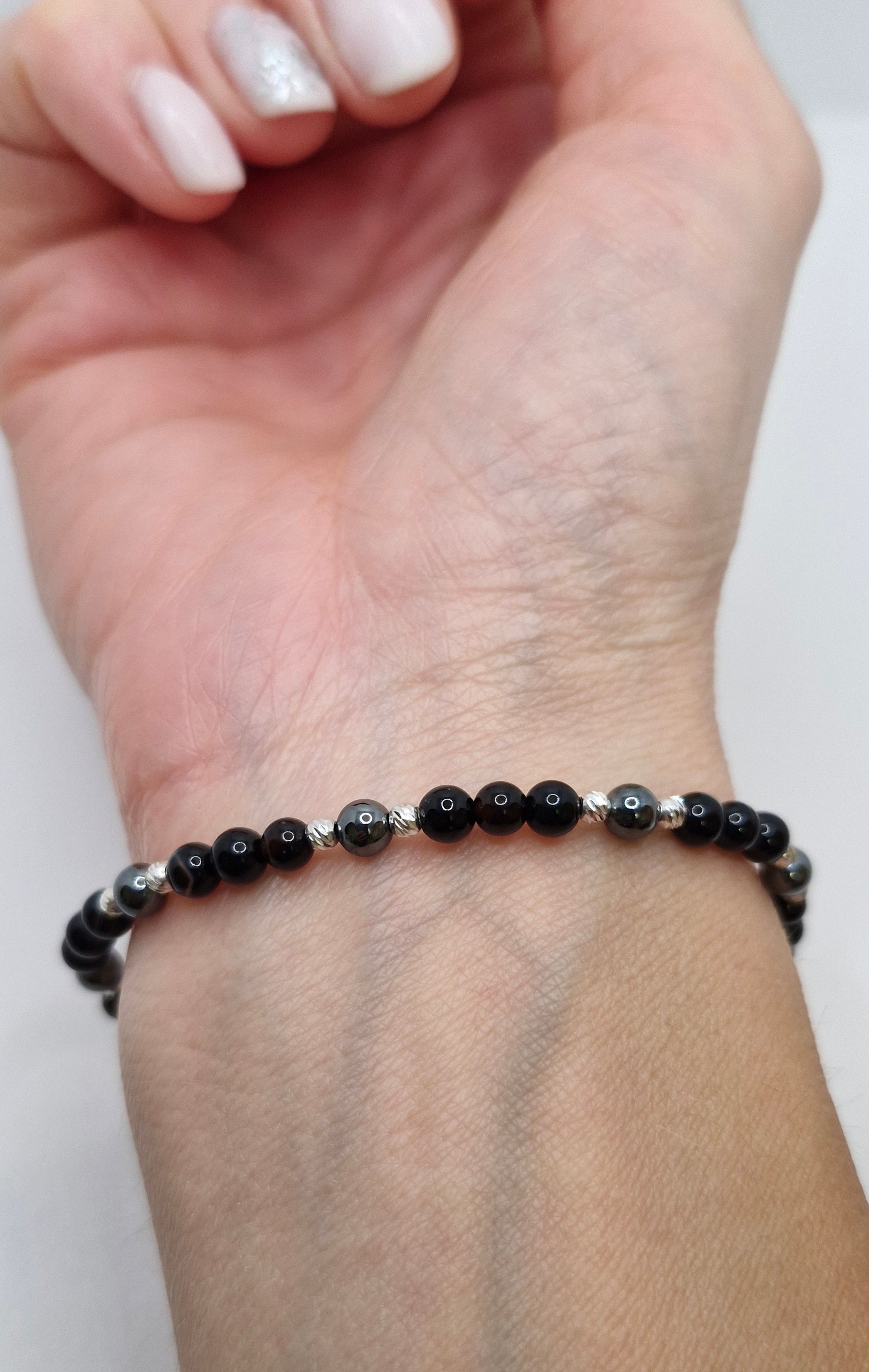 Black beaded bracelet on a wrist with a plain background