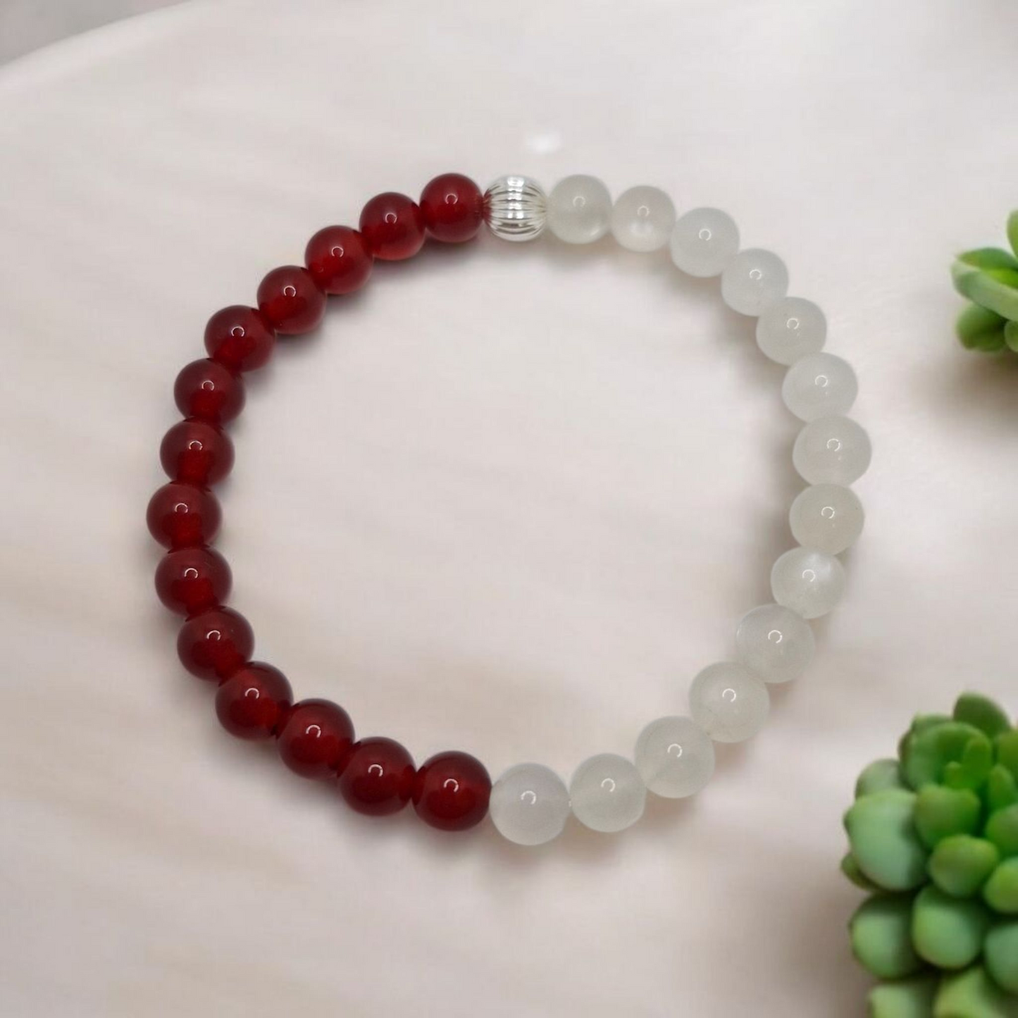 Beaded bracelet with red and white beads on a white surface with green plants.