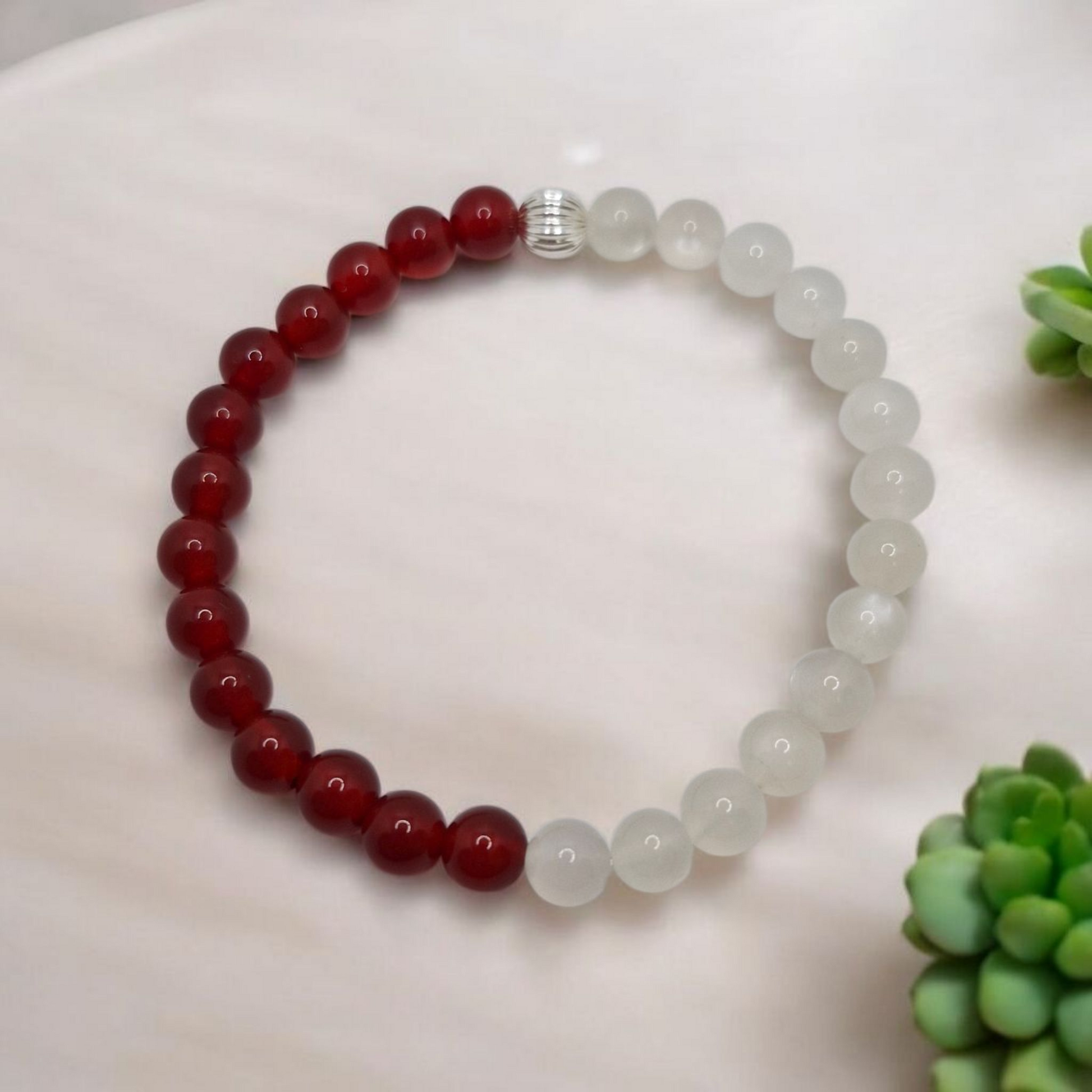 Beaded bracelet with red and white beads on a white surface with green plants.