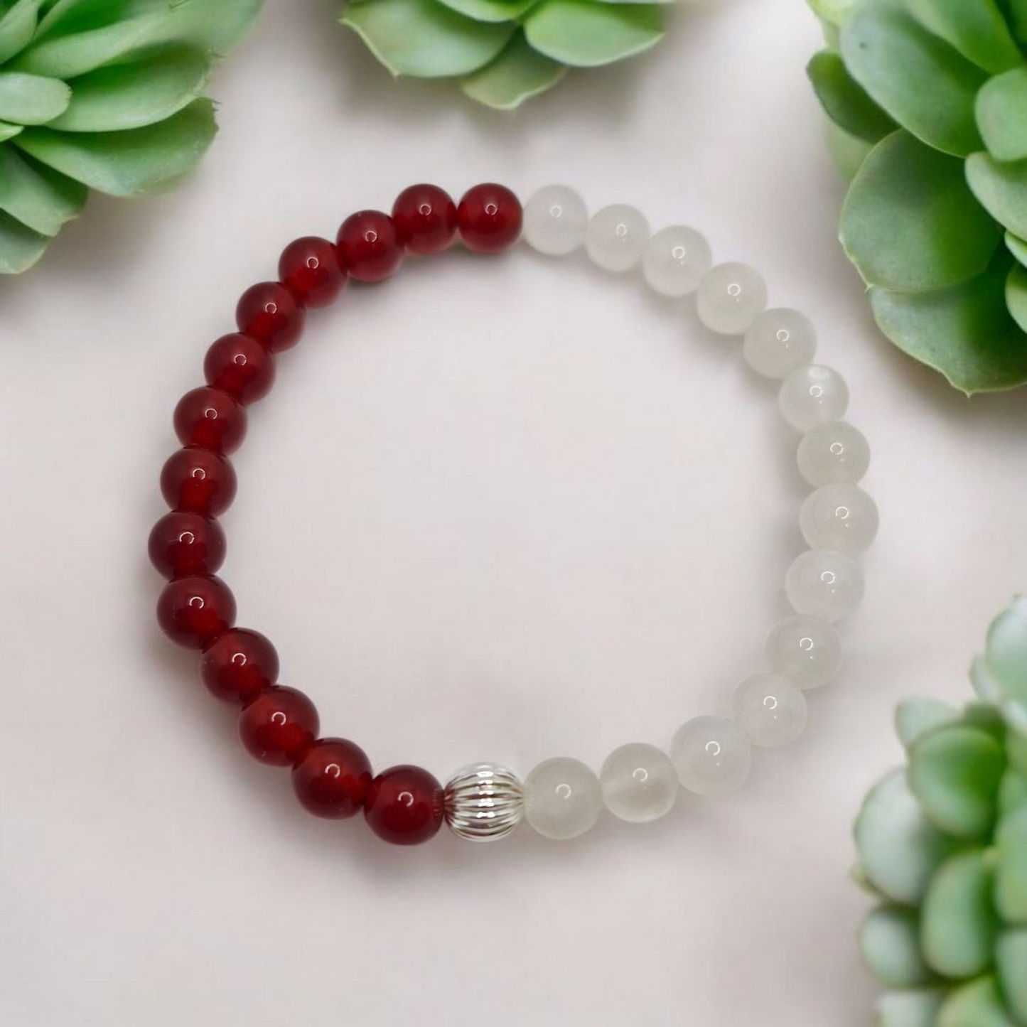 Beaded bracelet with red and clear beads on a light surface with green succulents.